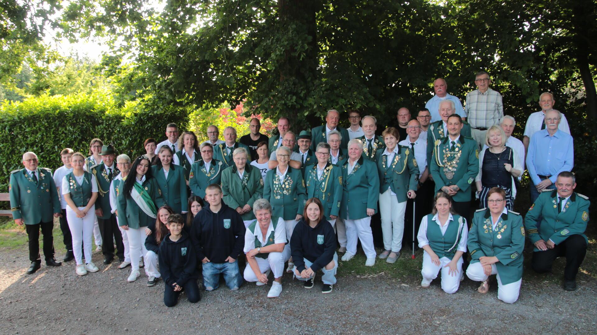 Gruppenfoto des Schützenvereins Drangstedt zum 150-jährigen Jubiläum: Über 40 Vereinsmitglieder und Gäste in grüner Schützenkleidung und Alltagskleidung posieren bei sonnigem Wetter vor einem Baum und dichten Hecken.