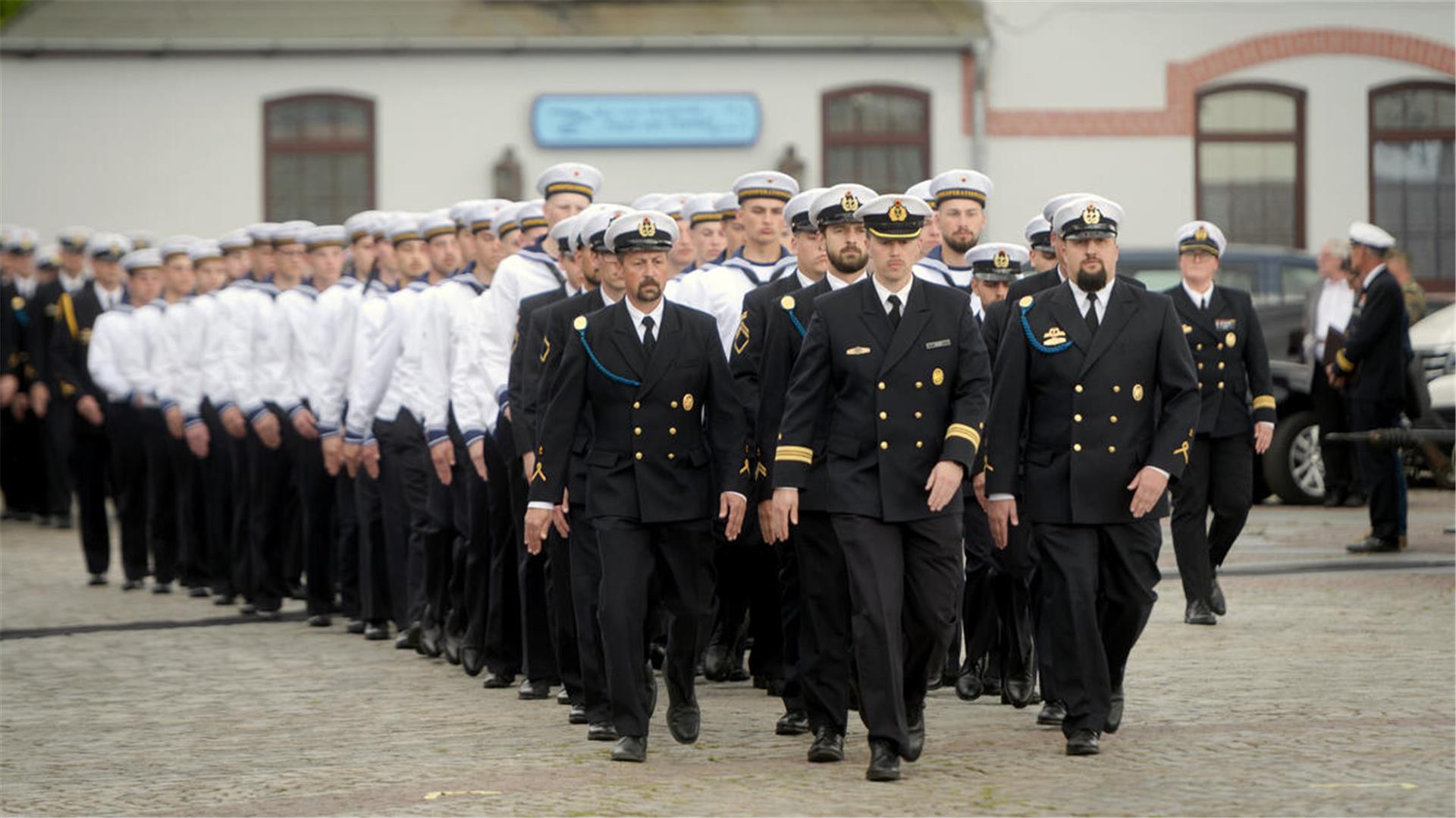 Rekrutinnen und Rekruten der der Marineoperationsschule Bremerhaven: Frauen und Männer in mal weißen oder dunkelblauen Marine-Uniformen marschieren einen Weg entlang.