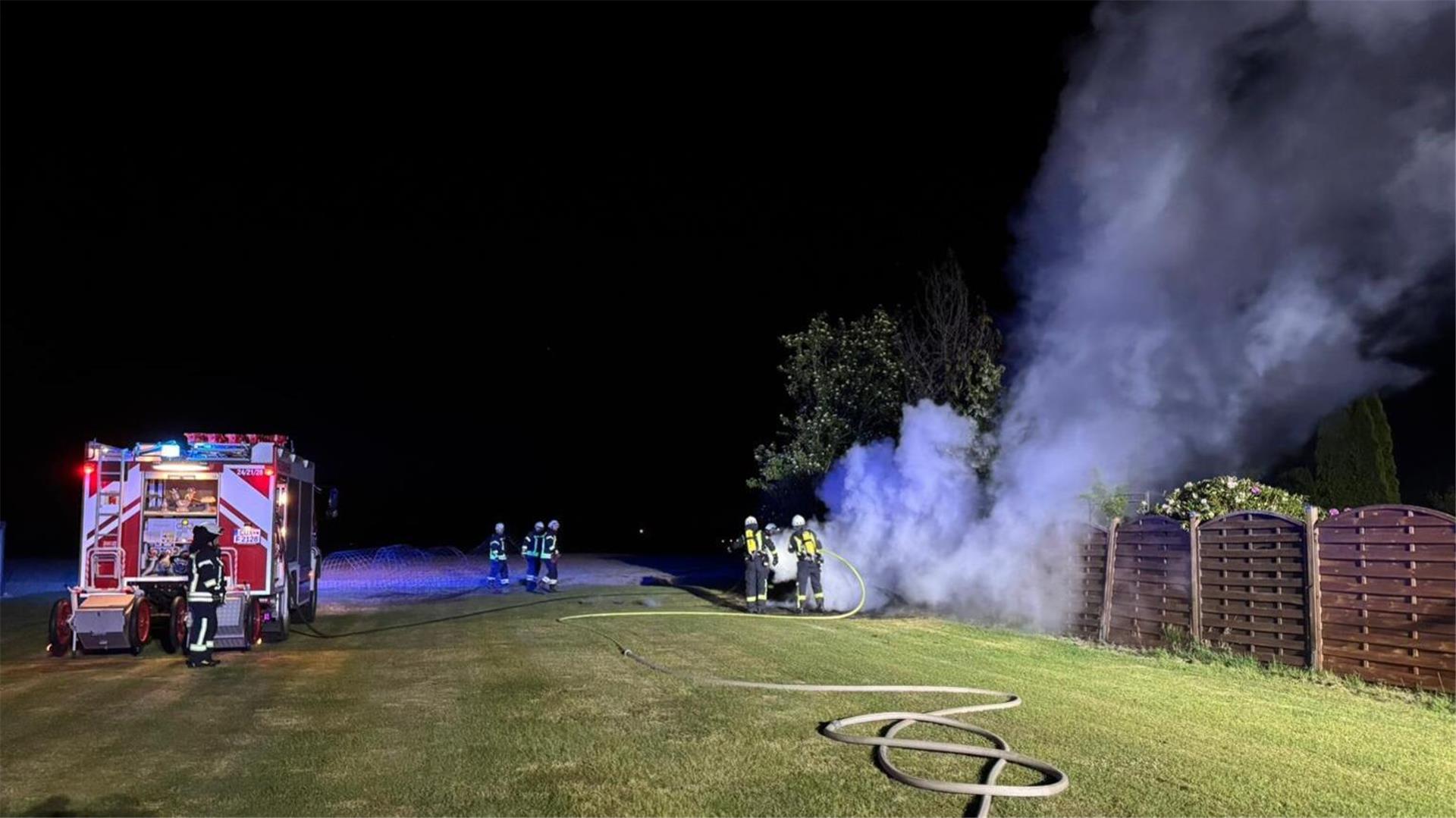 Einsatzkräfte der Feuerwehr löschen einen brennenden Holzstapel.