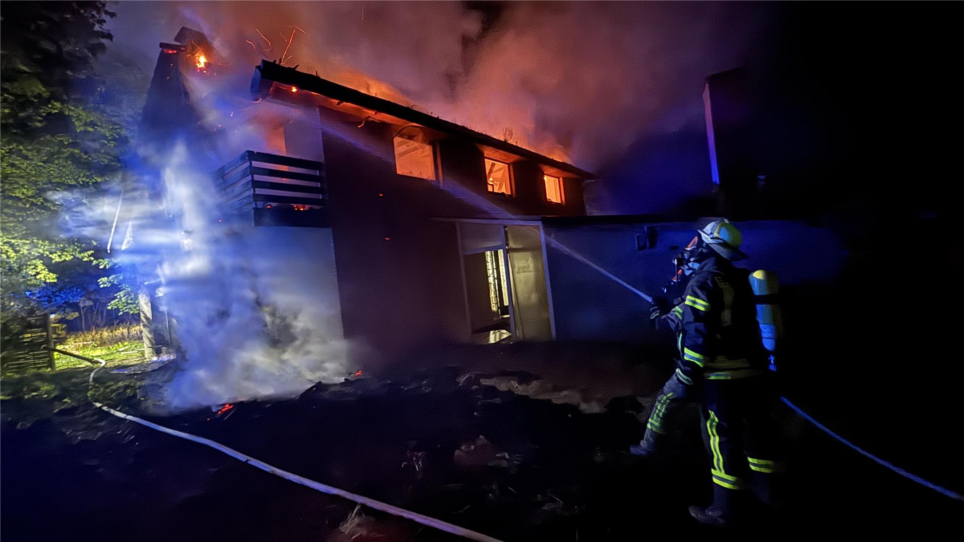 Feuerwehrleute löschen ein brennendes Haus.