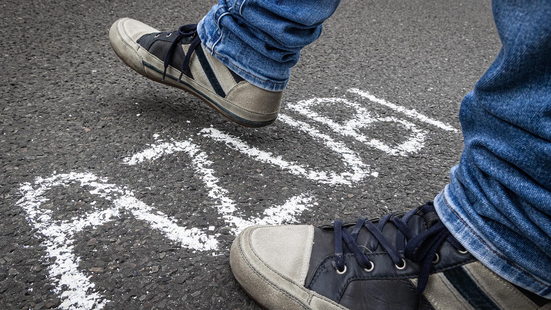 Ein Mann geht in Turnschuhen über einen Schriftzug. Mit weißer Farbe steht "Azubi" auf den Boden geschrieben. 