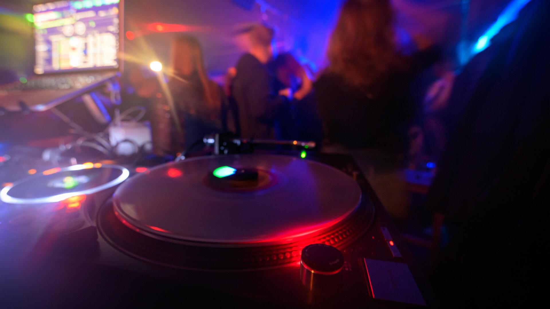 Partygänger tanzen vor einem DJ-Pult in einem Club.