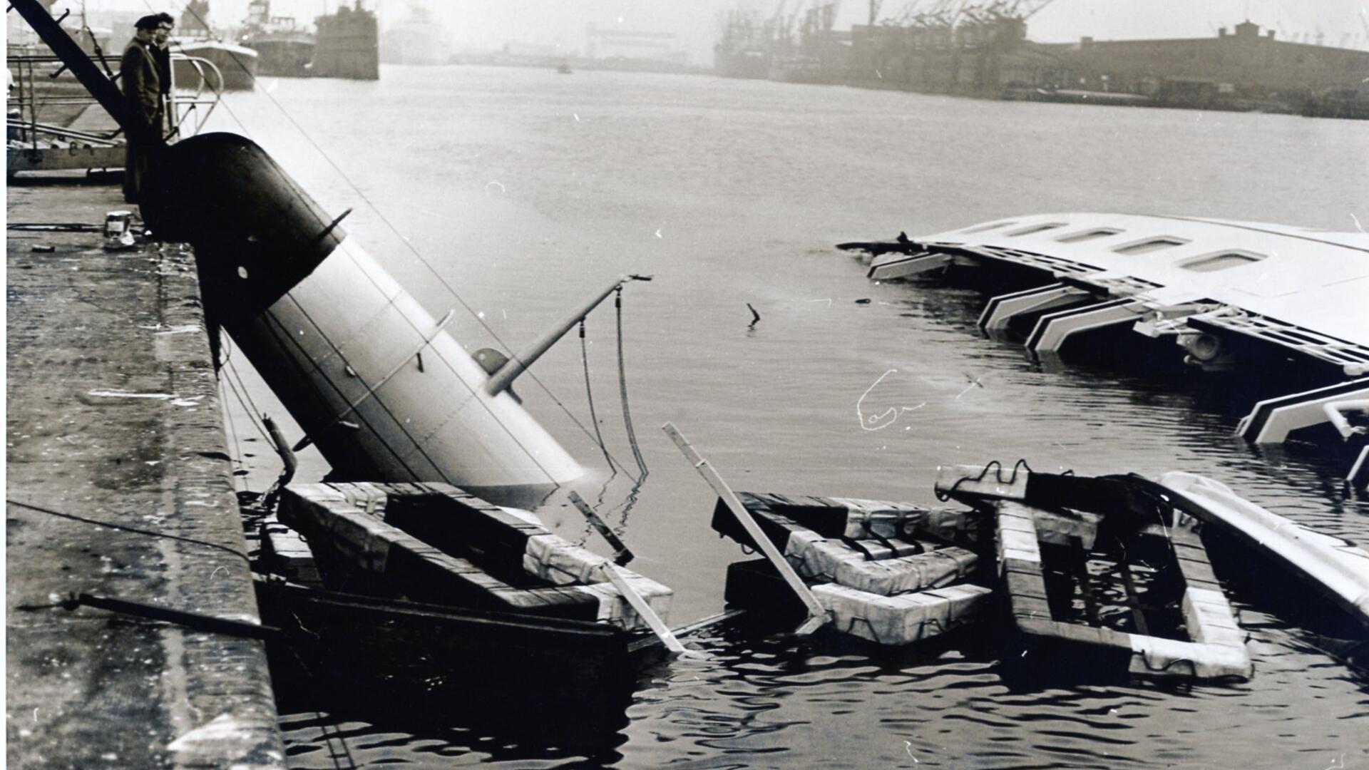 Am Morgen nach dem Unglück gluckerte es noch im Rumpf des Schiffs. Rettungsflöße schwammen im Wasser, und der abgeknickte Schornstein lehnte an der Kajenmauer. Unter den nun waagerechten Fenstern des Hauptdecks leuchtete das Rot der Schwimmwesten, die unter den Fenstern im Inneren der „Bremerhaven" im Wasser dümpelten.