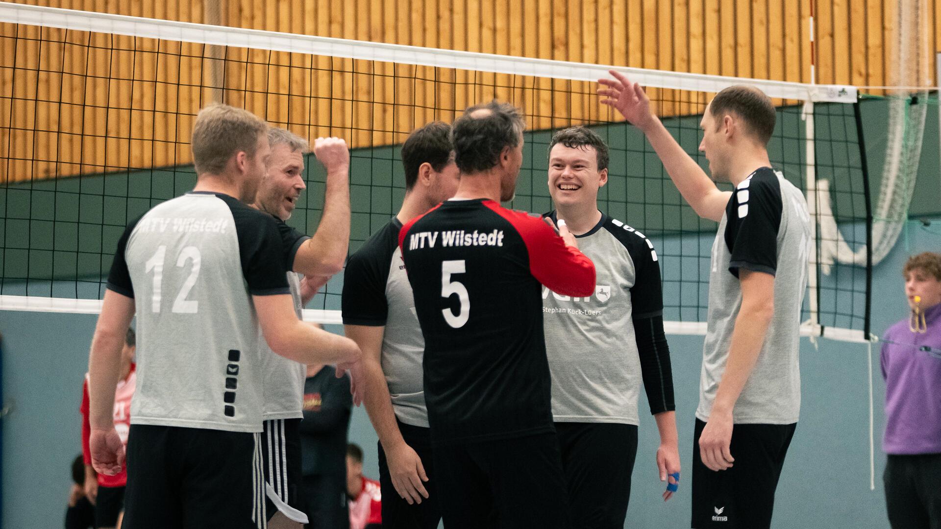 Männer stehen vor einem Volleyballnetz und jubeln. 