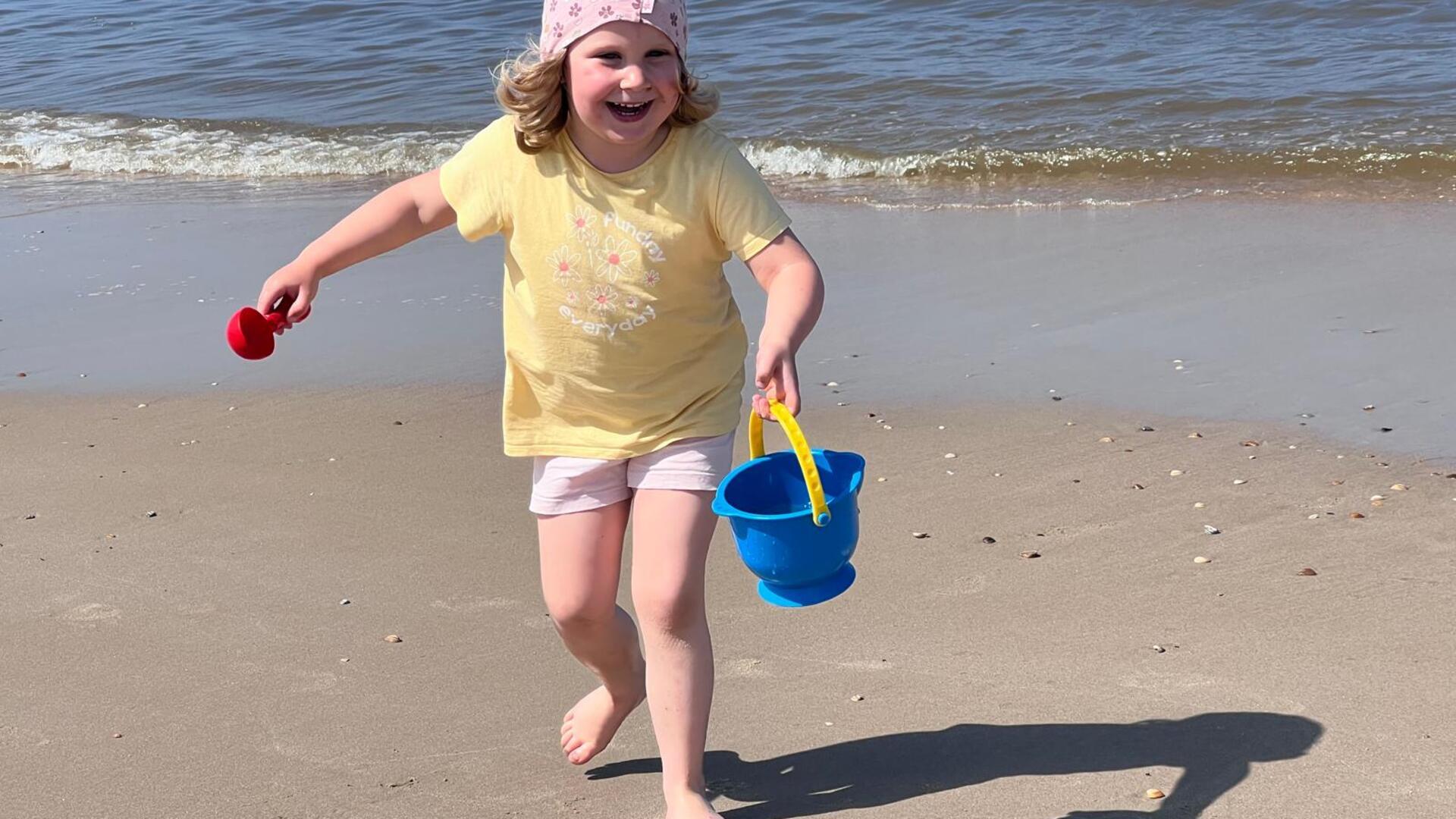 Ein kleines lachendes Mädchen, das am Strand spielt.