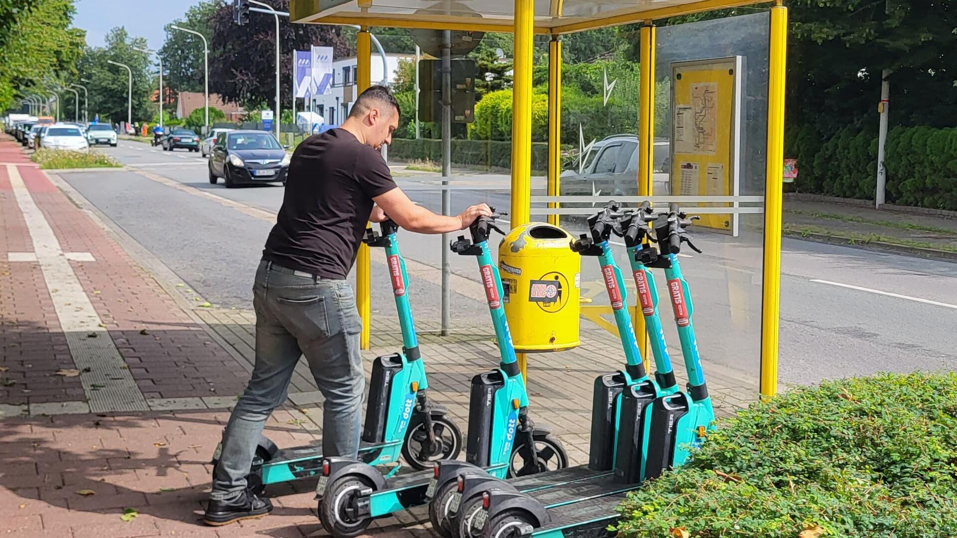 Ein Mann stellt E-Scooter an einer Bushaltestelle auf. 