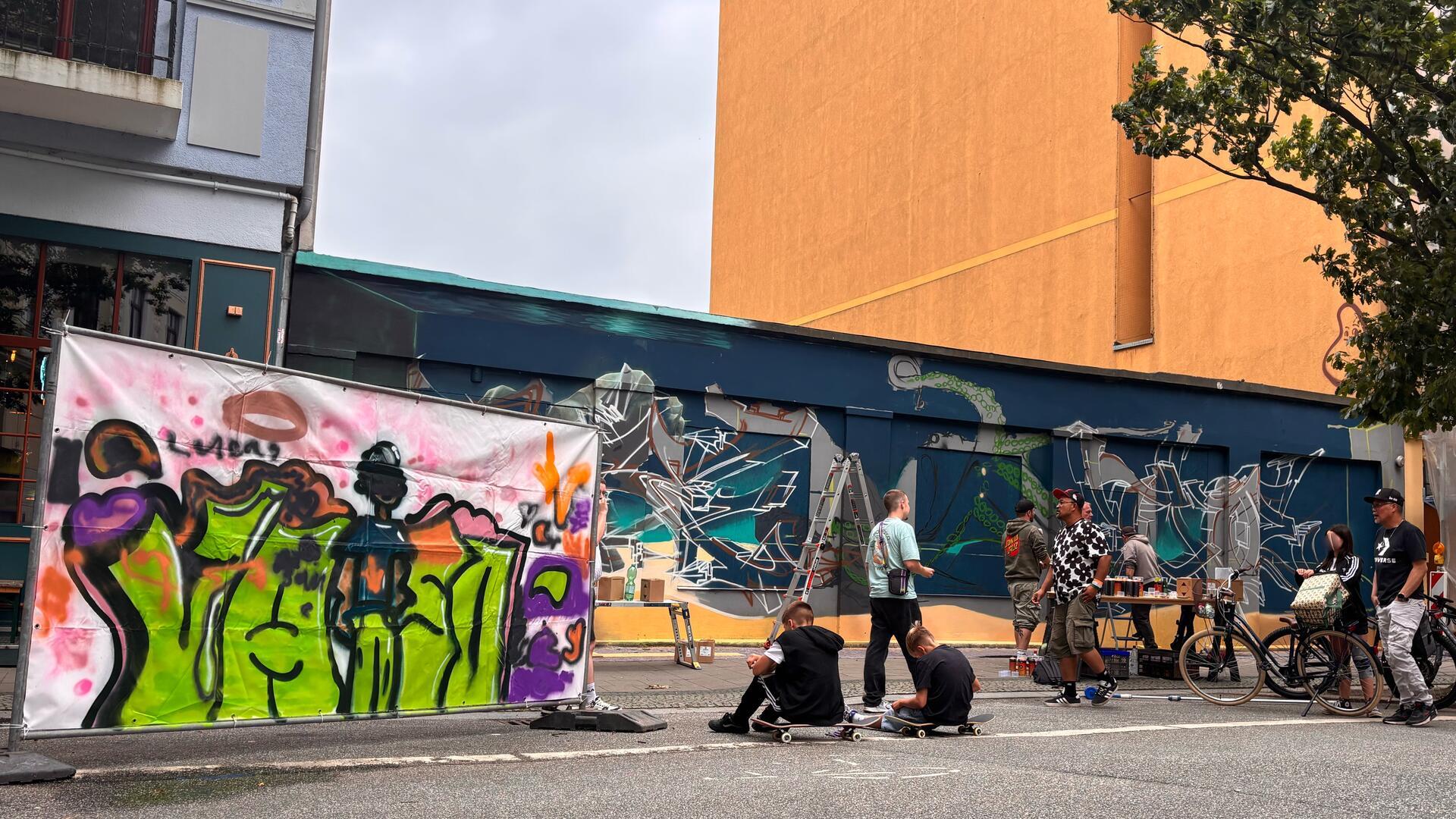 Menschen vor einer Wand, an der Graffiti gesprüht wird.