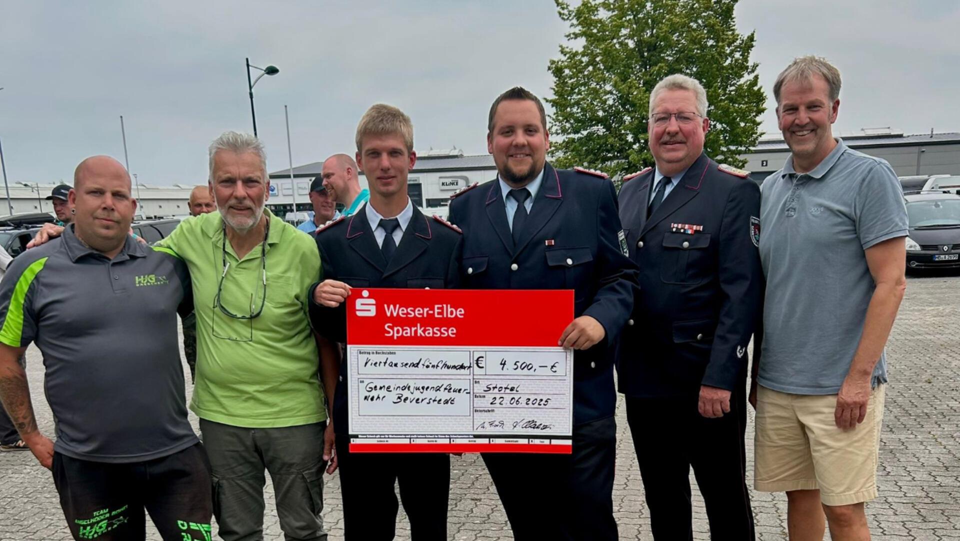 Gruppenfoto mit sechs Männern, darunter Vertreter der Feuerwehr in Uniform, die einen symbolischen Scheck über 4.500 Euro für die Jugendfeuerwehr Beverstedt präsentieren.