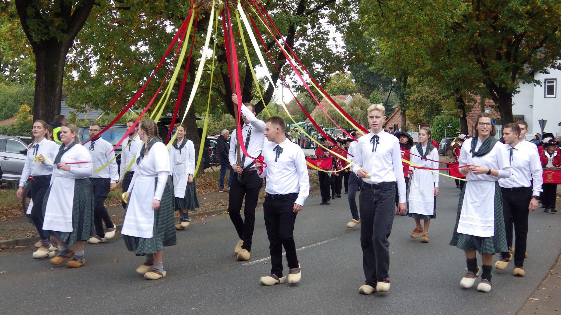 Junge Männer und Frauen in weißen Hemden halten bunte Bänder in den Händen.