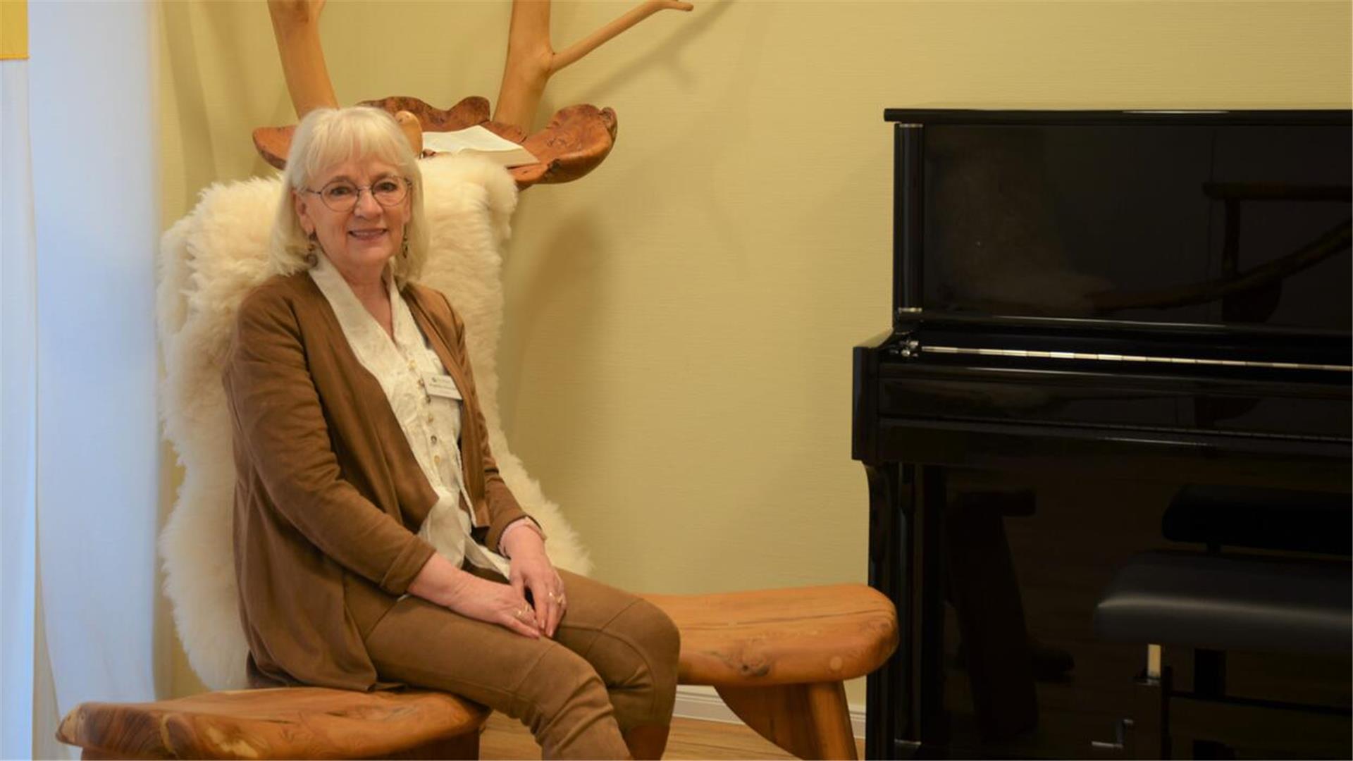 Eine Frau sitzt auf einer Holzbank neben einem Klavier.