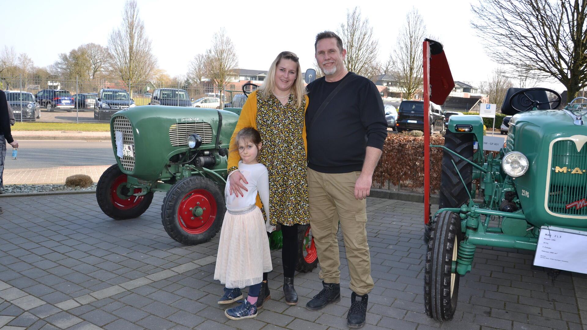 Eine Frau und ein Mann stehen mit ihrer kleinen Tochter vor einem historischen Schlepper.