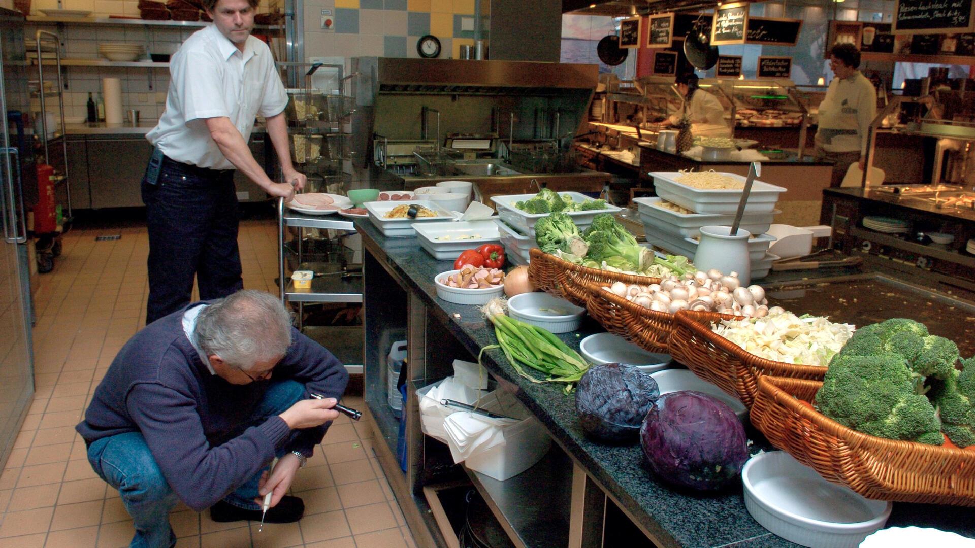 Ein Mann hockt mit einer Taschenlampe in einer Restaurantküche.