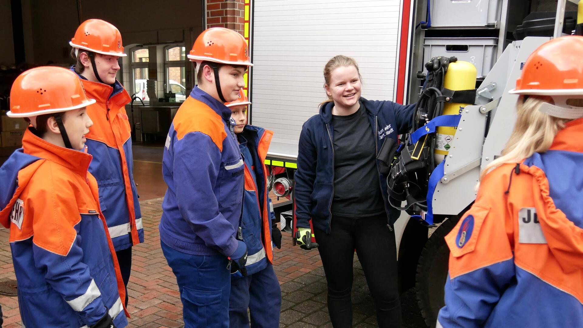 Junge Menschen stehen in einer Gruppe zusammen. Einige von ihnen tragen Feuerwehrdienstkleidung.