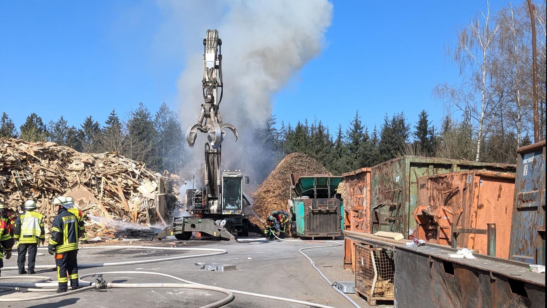 Ein Bagger qualmt. Feuerwehrleute stehen zur Löschung bereit.