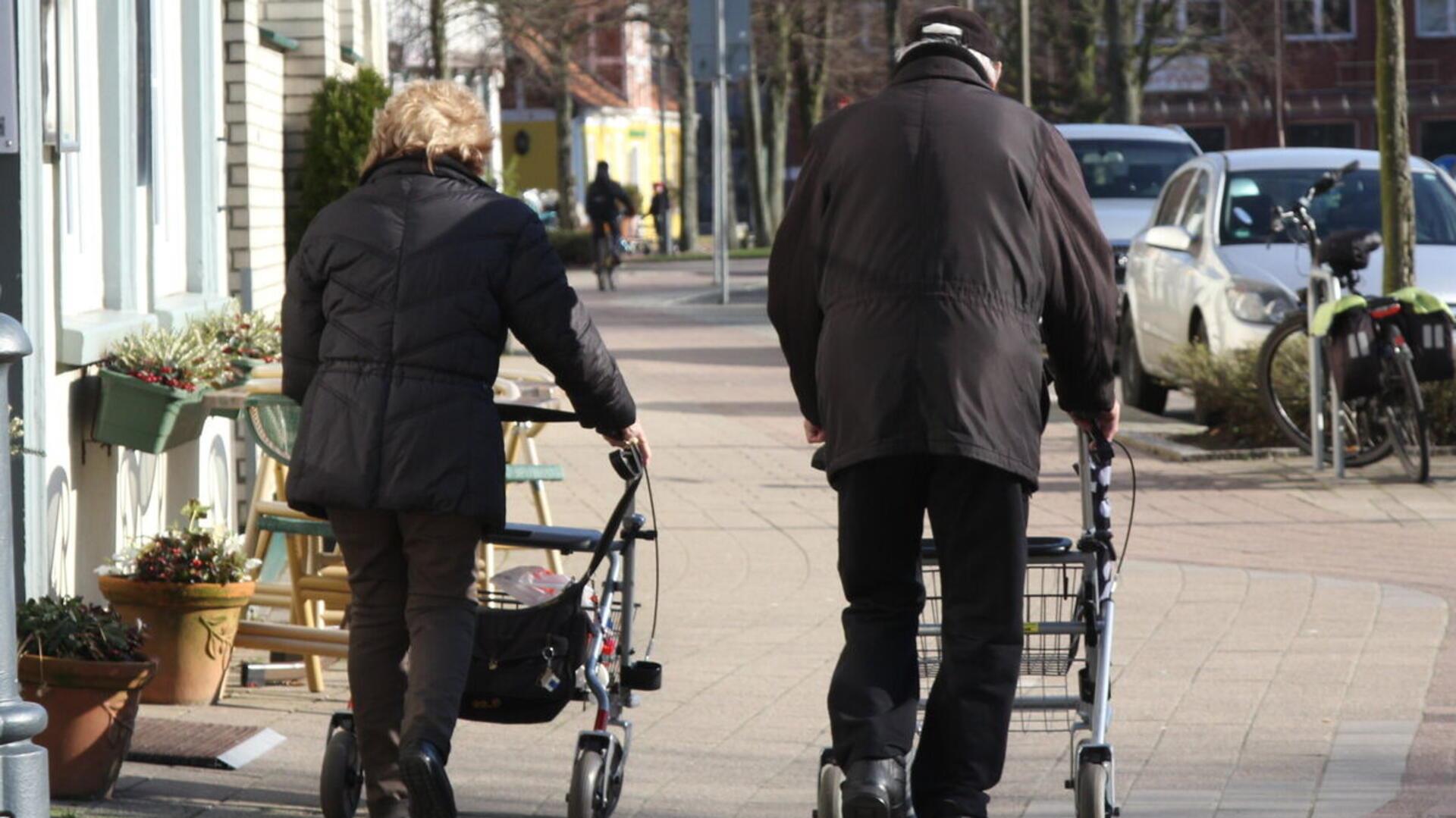 Zwei ältere Menschen schieben ihren Rollator über den Fußweg.
