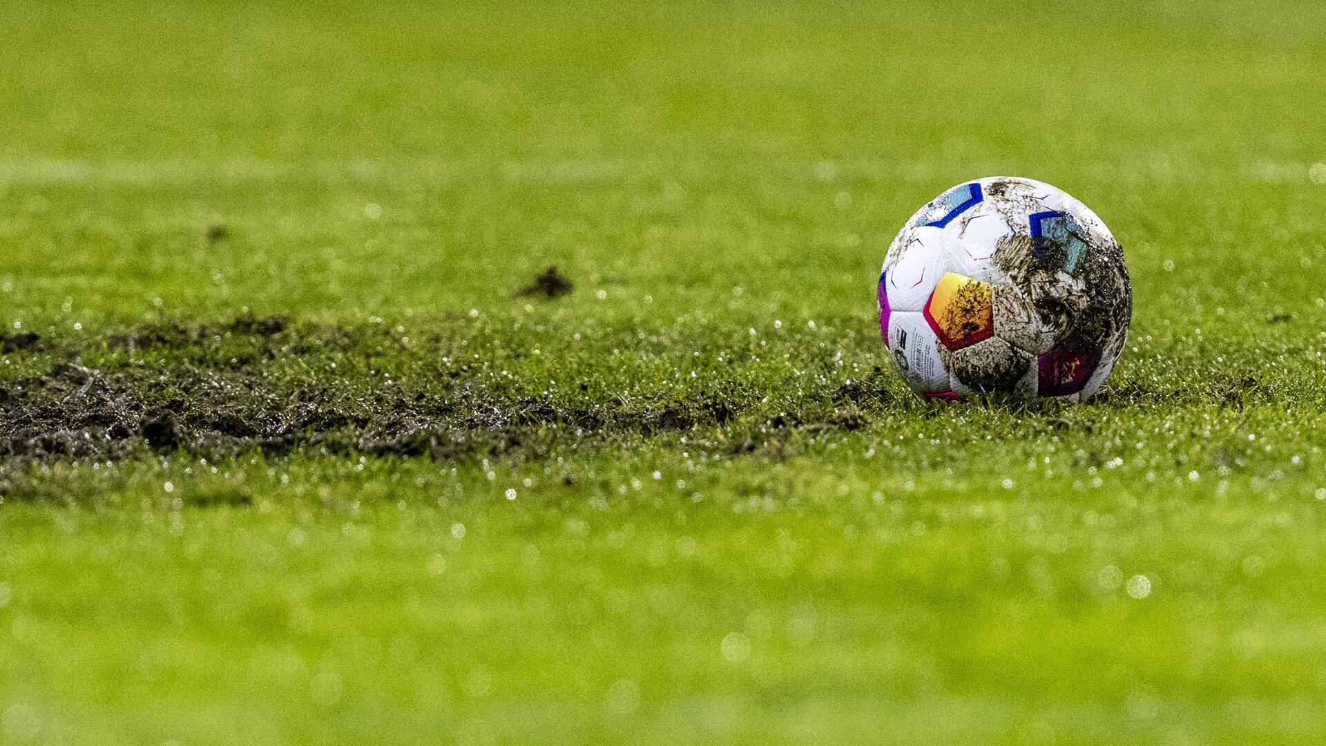 Ein Fußball liegt am Elfmeterpunkt im matschigen Rasen.