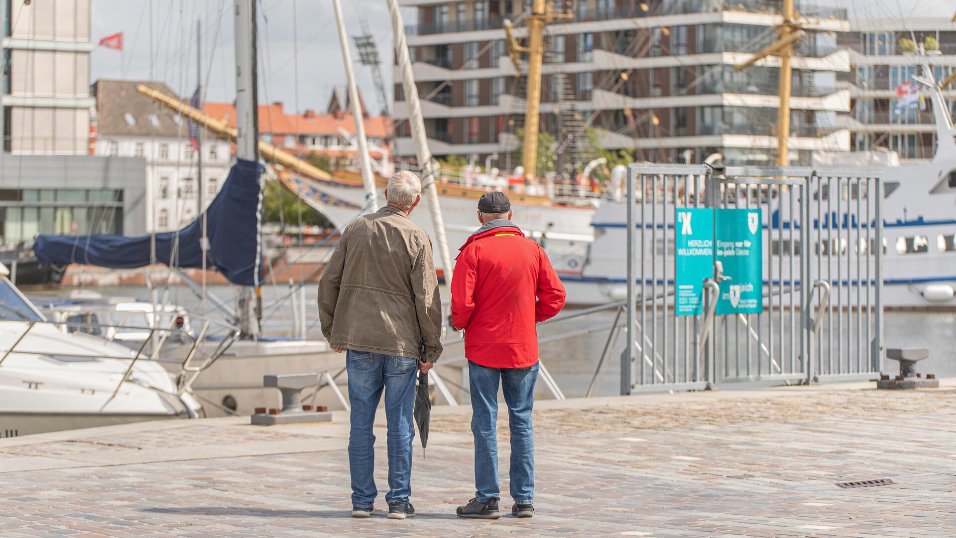 Zwei Männer blicken auf den neuen Hafen. Aus der Ferne wirkt der Hafen idyllisch, doch es gibt noch Baustellen.