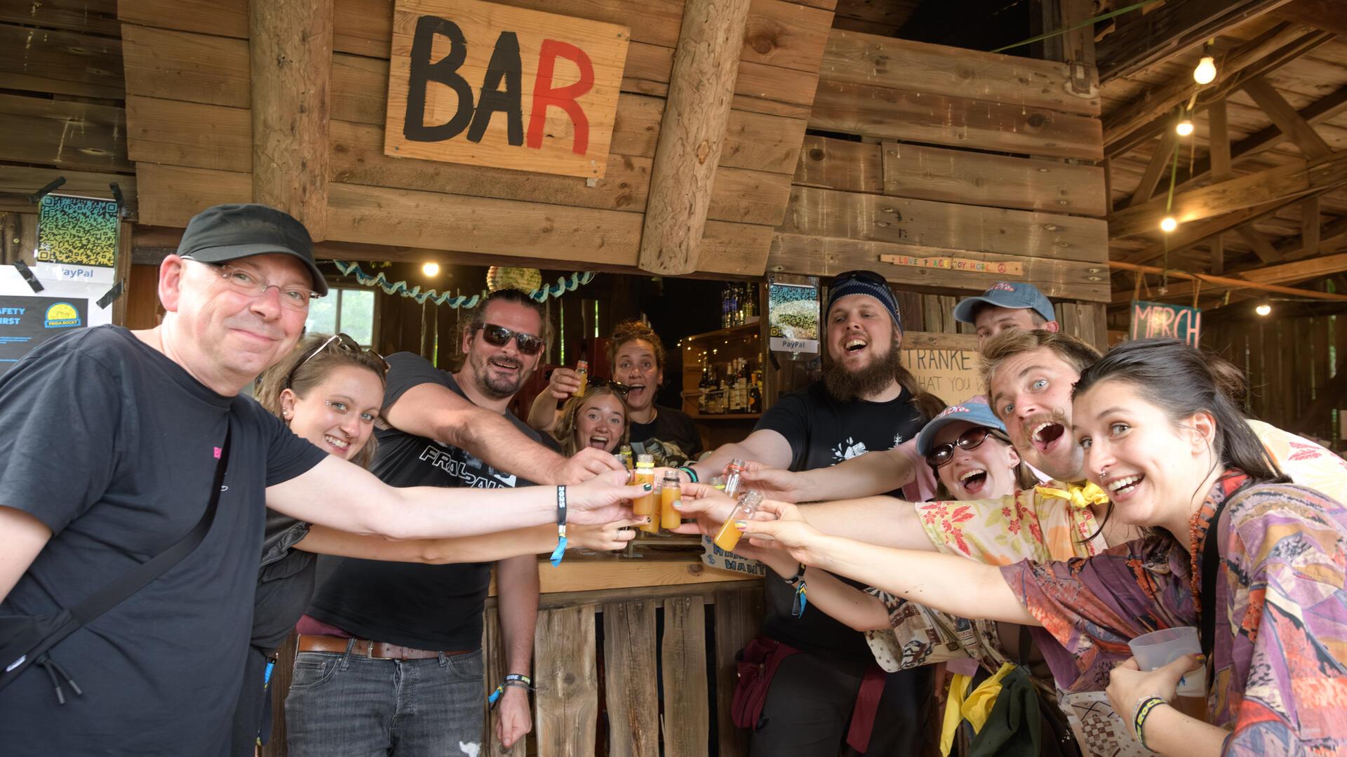 Mehrere Menschen feiern ausgelassen beim Festival "Frida rockt". Hier stoßen sie gemeinsam vor der Bar an.