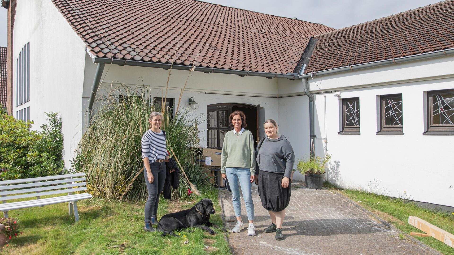 Drei Frauen und ein Hund vor einer Kirche im Umbau zur Tierarztpraxis.