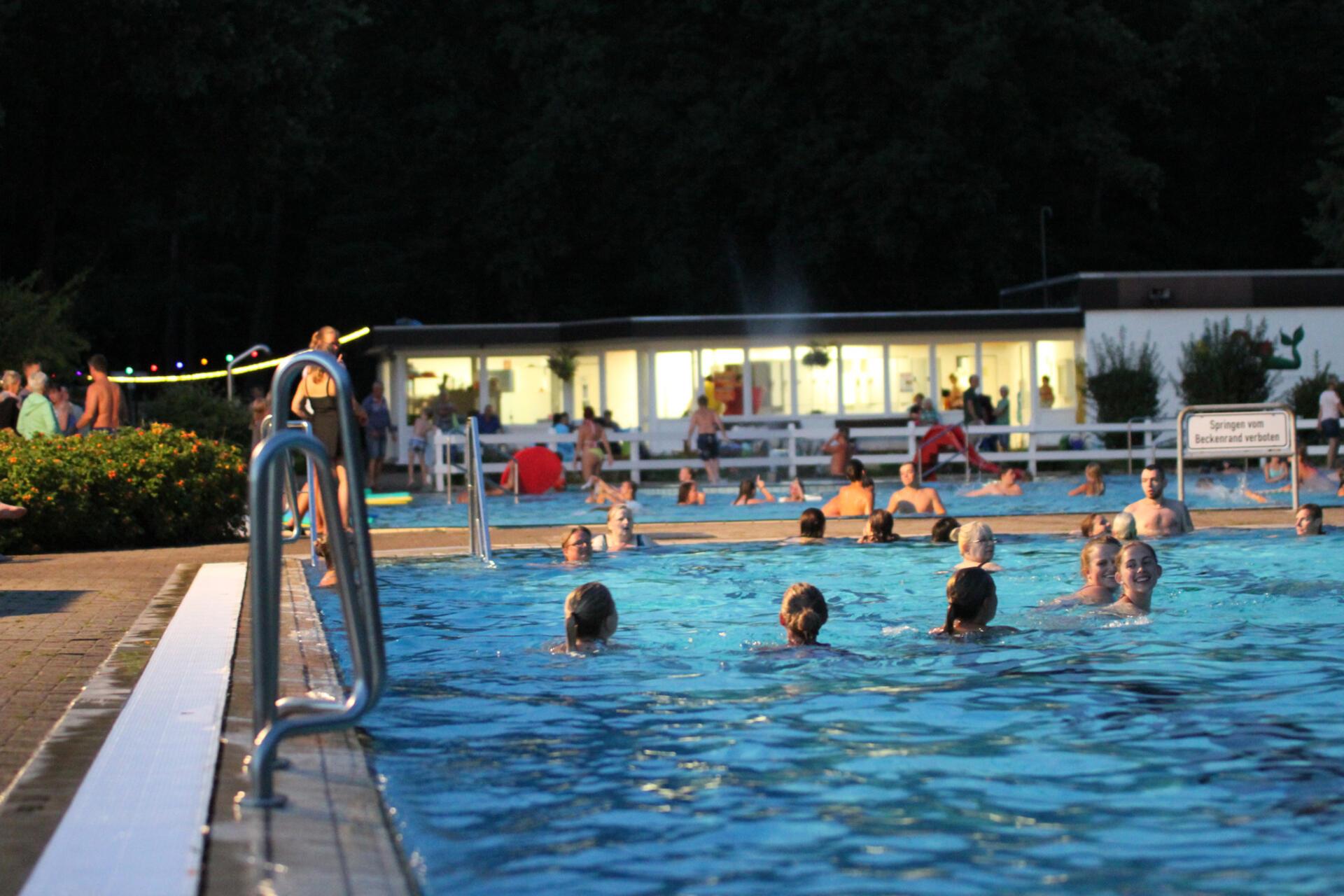 Menschen schwimmen unter Flutlicht. Das Flutlichtbaden ist die Hauptattraktion in Hepstedt.