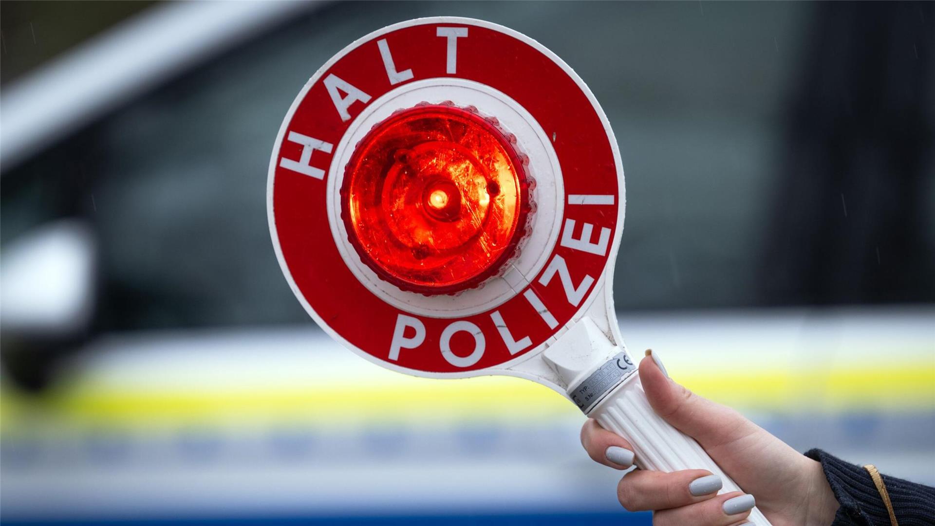 Eine Polizistin hält während einer Verkehrskontrolle eine Polizeikelle mit der Aufschrift „Halt Polizei“.