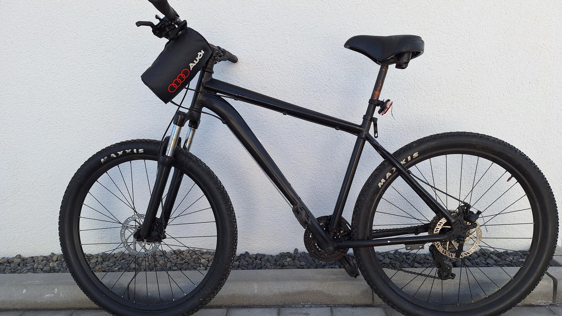 Ein schwarz lackiertes Fahrrad lehnt an einer weißen Wand. 