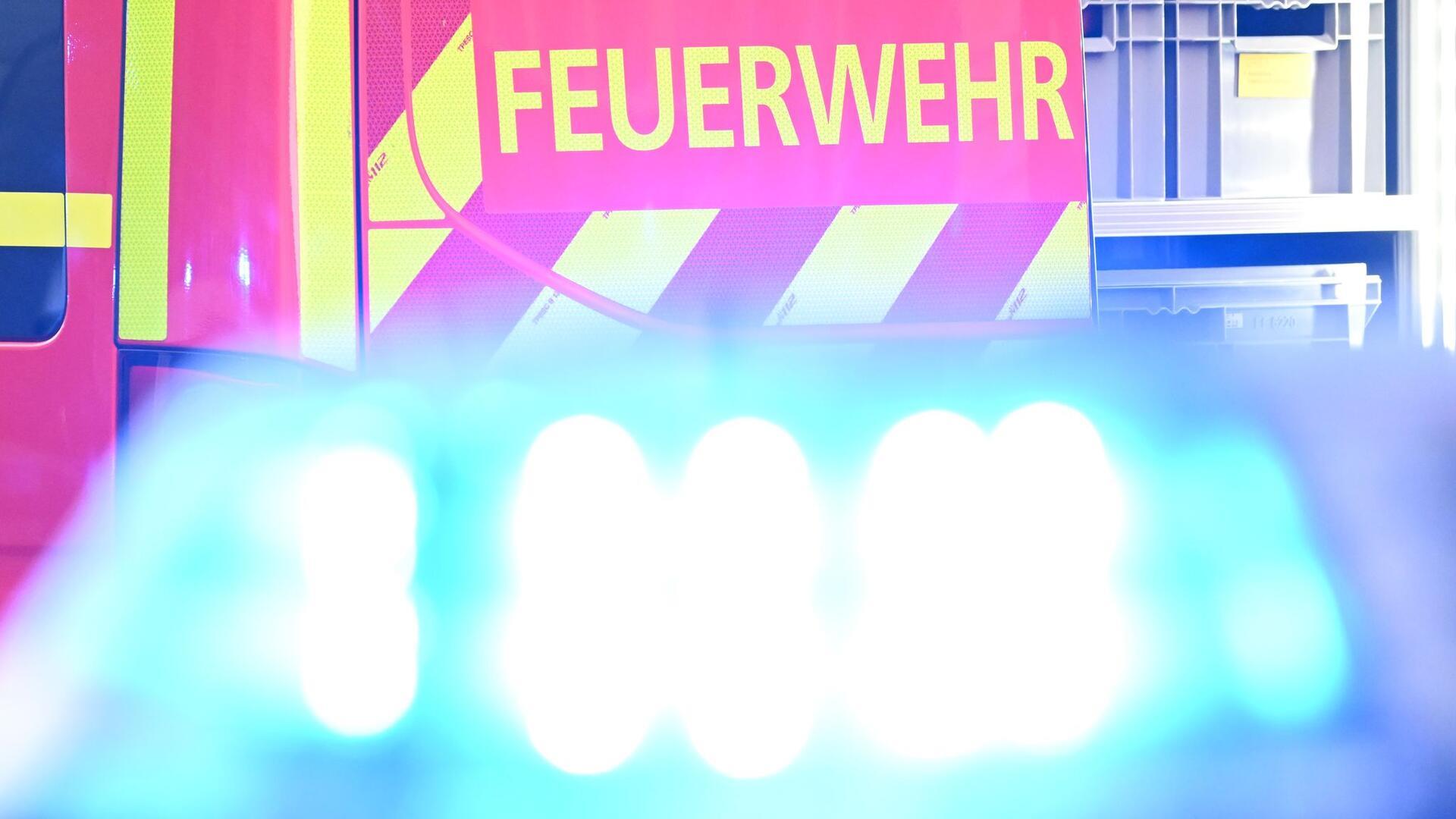 Ein Fahrzeug der Feuerwehr steht bei einem Einsatz auf einer Straße, während im Vordergrund das Blaulicht eines Polizeifahrzeugs zu sehen ist. 