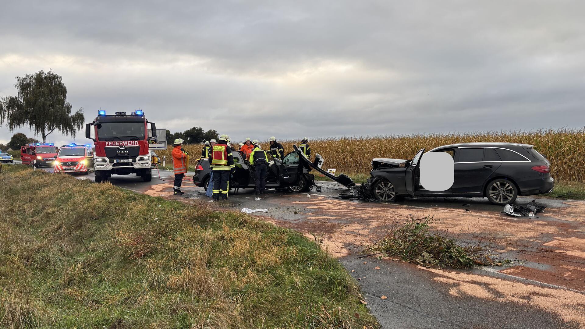 Mehrere Einsatzfahrzeuge von Feuerwehr, Rettungsdienst und Polizei stehen auf einer von einem Verkehrsunfall verwüsteten Landstraße. Im Vordergrund sind zwei durch die Kollision schwer beschädigte Pkw zu sehen.