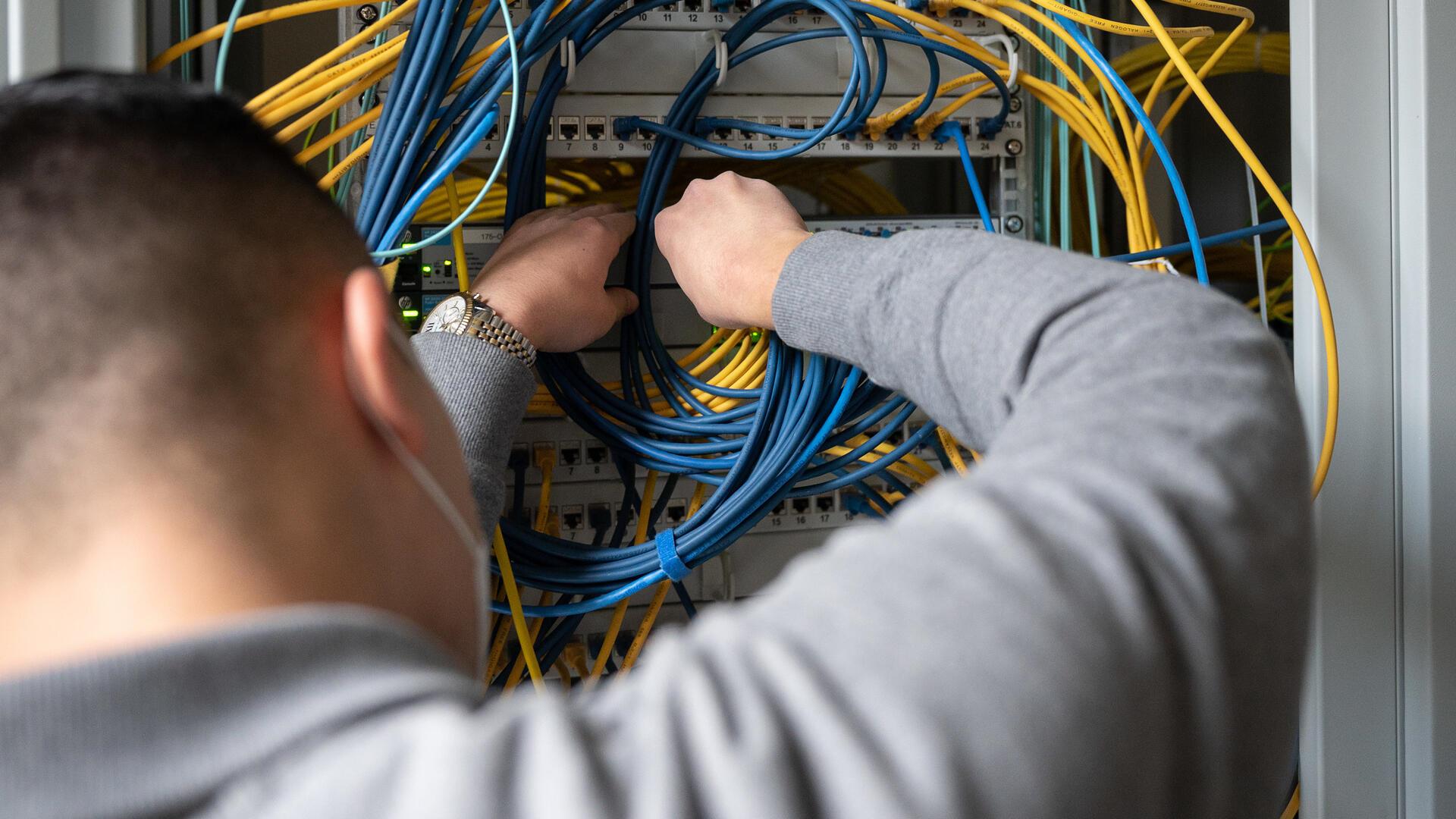 Ein Auszubildender für Fachinformatik und Systemintegration steckt an einem Server ein Netzwerkkabel ein. 