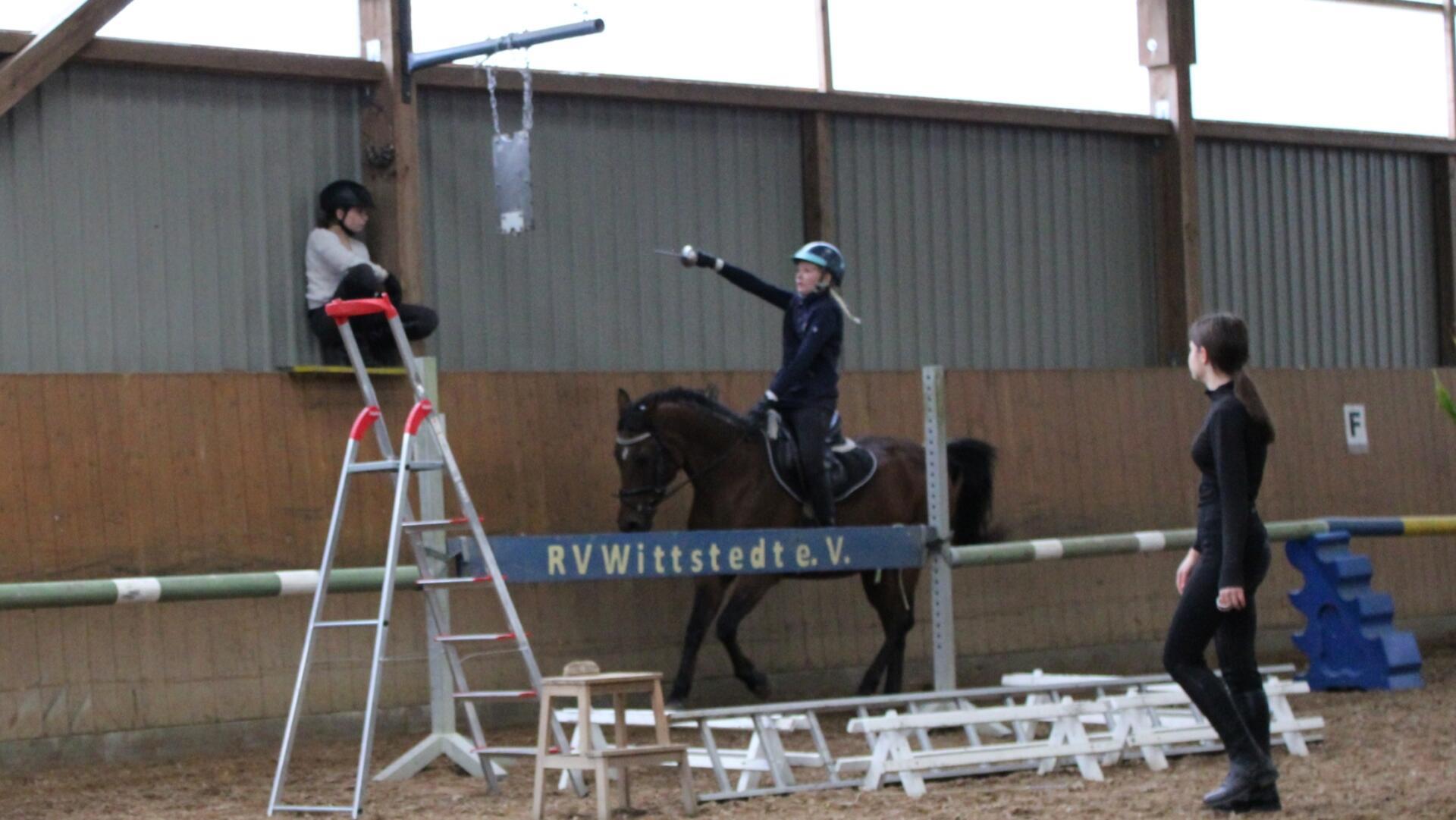 Szene beim Ringreiten: Zwei Personen und ein Pferd mit Reiterin.