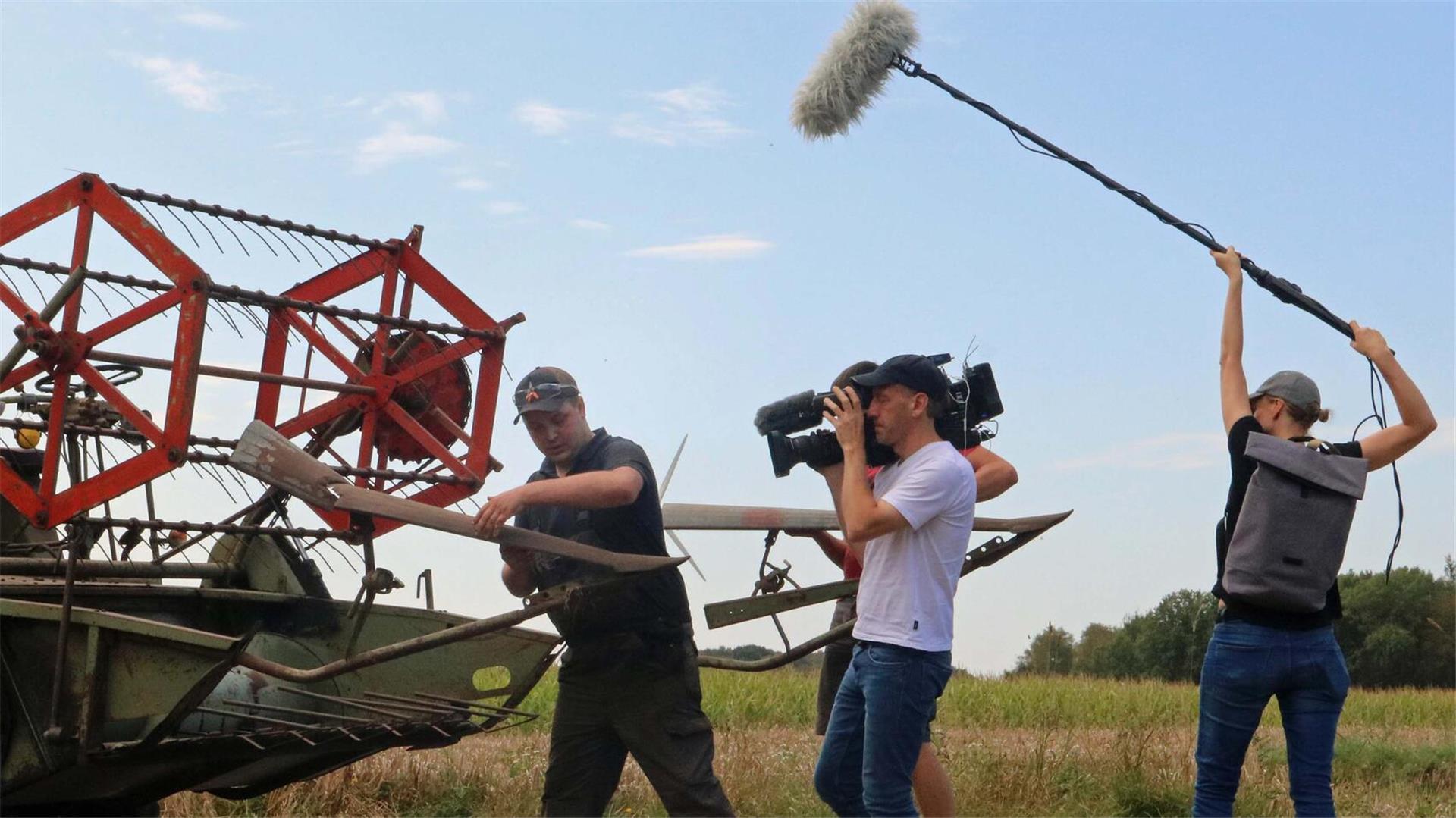 Ein Mann an einem Mähdrescher wird von einem Kamerateam gefilmt.