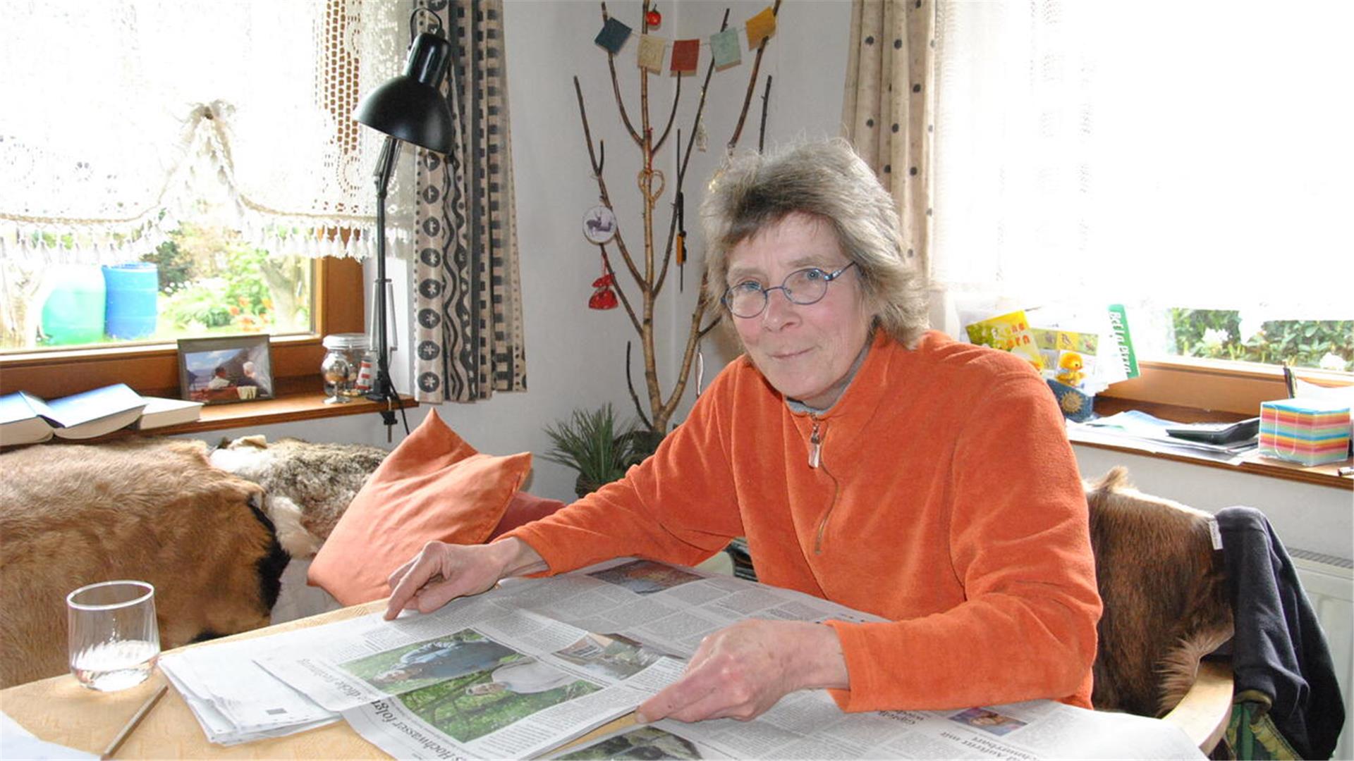 Eine Frau sitzt am Tisch und hält eine Zeitung in Händen.