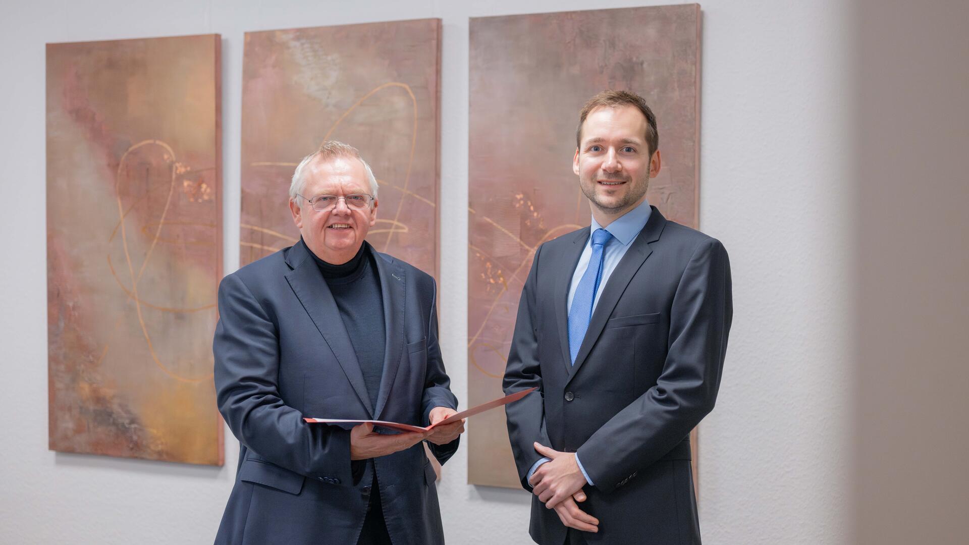 Zwei Männer vor einer Wand Übergabe Ernennungsurkunde