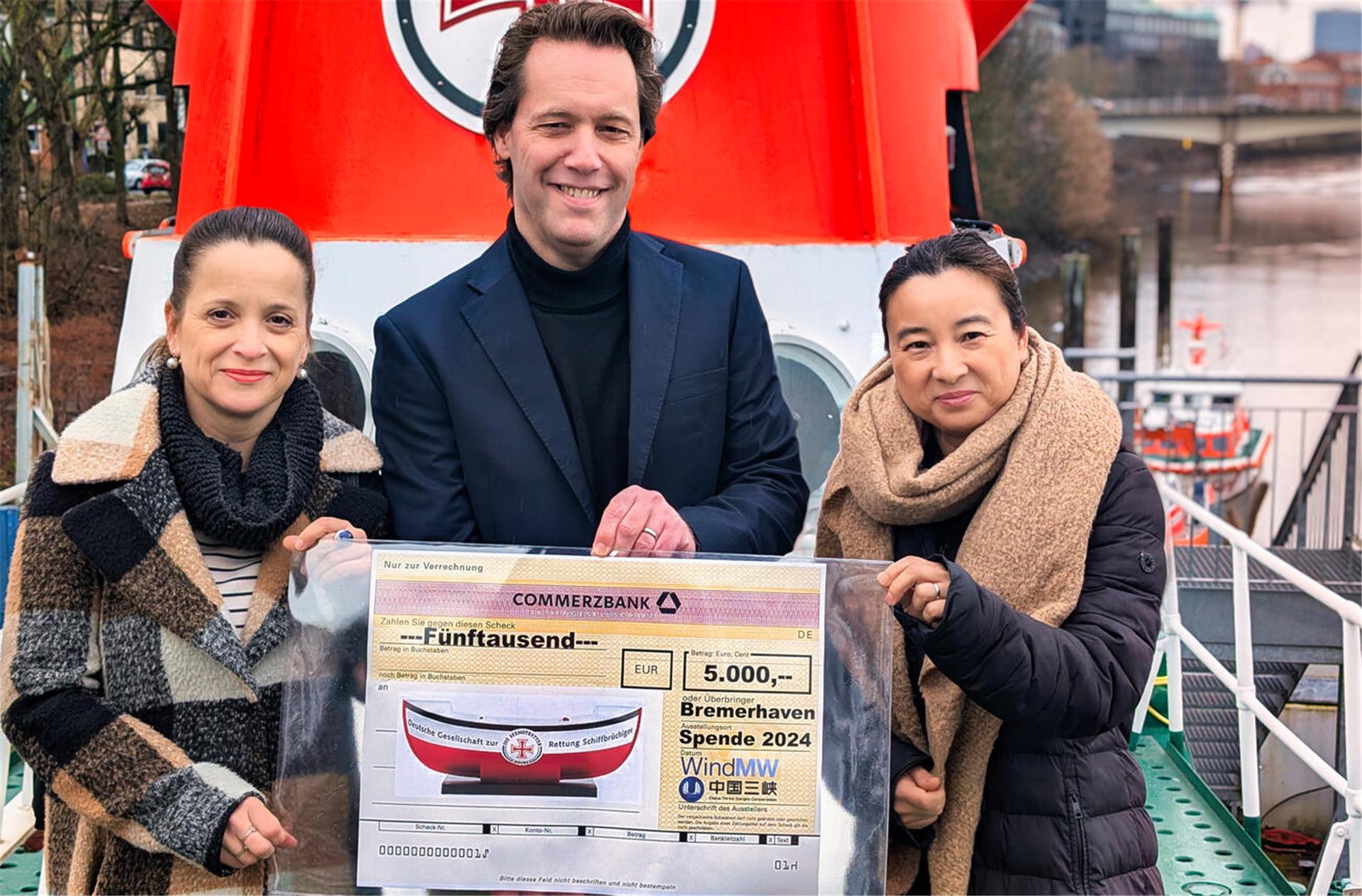 Zwei Vertreterinnen des Unternehmens WindMW halten gemeinsam mit einem Vertreter der DGzRS einen symbolischen Scheck in Höhe von 5.000 Euro hoch. 