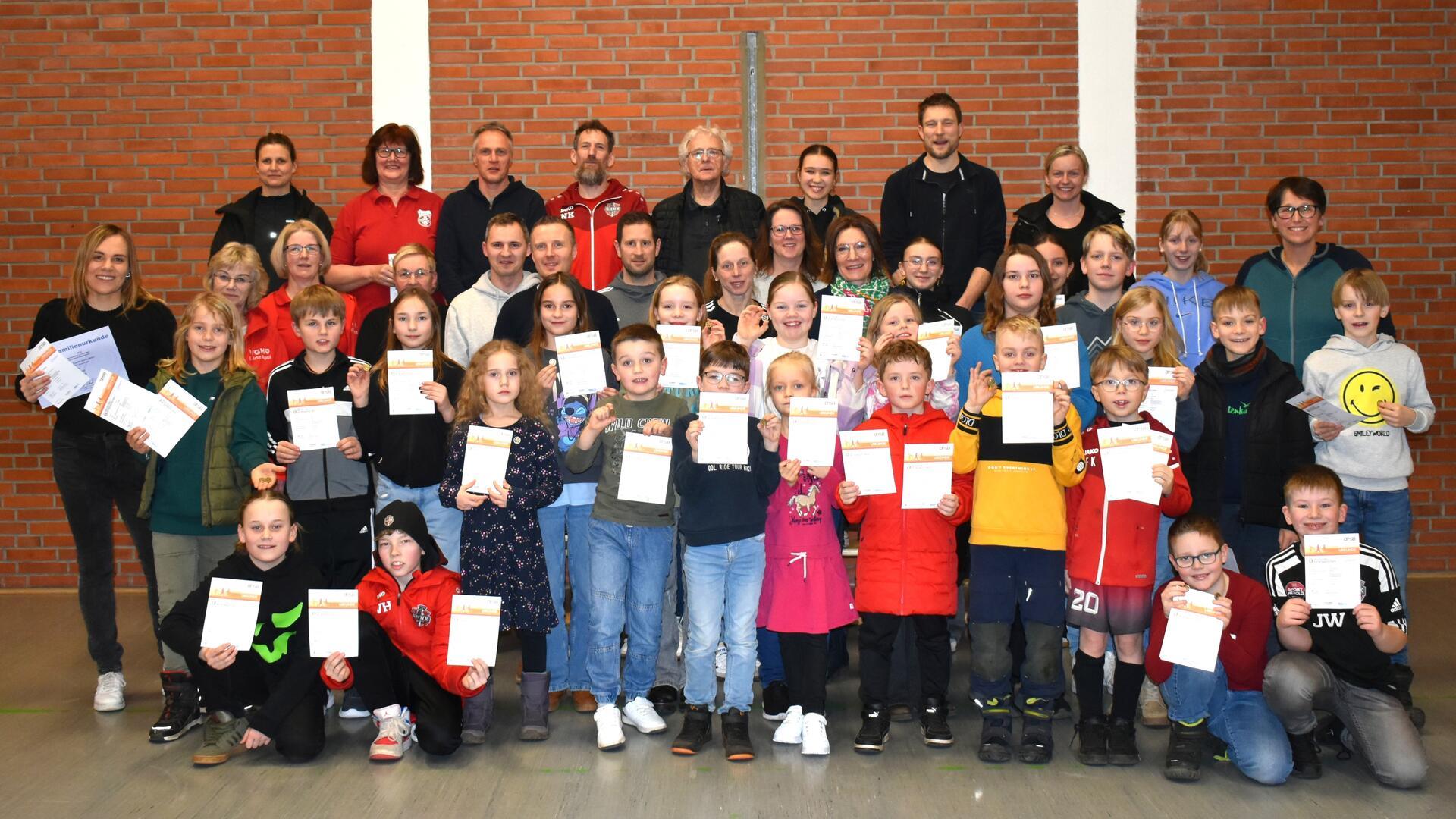 Erwachsene und Kinder stehen in einer Gruppe. In den Händen halten sie Urkunden.