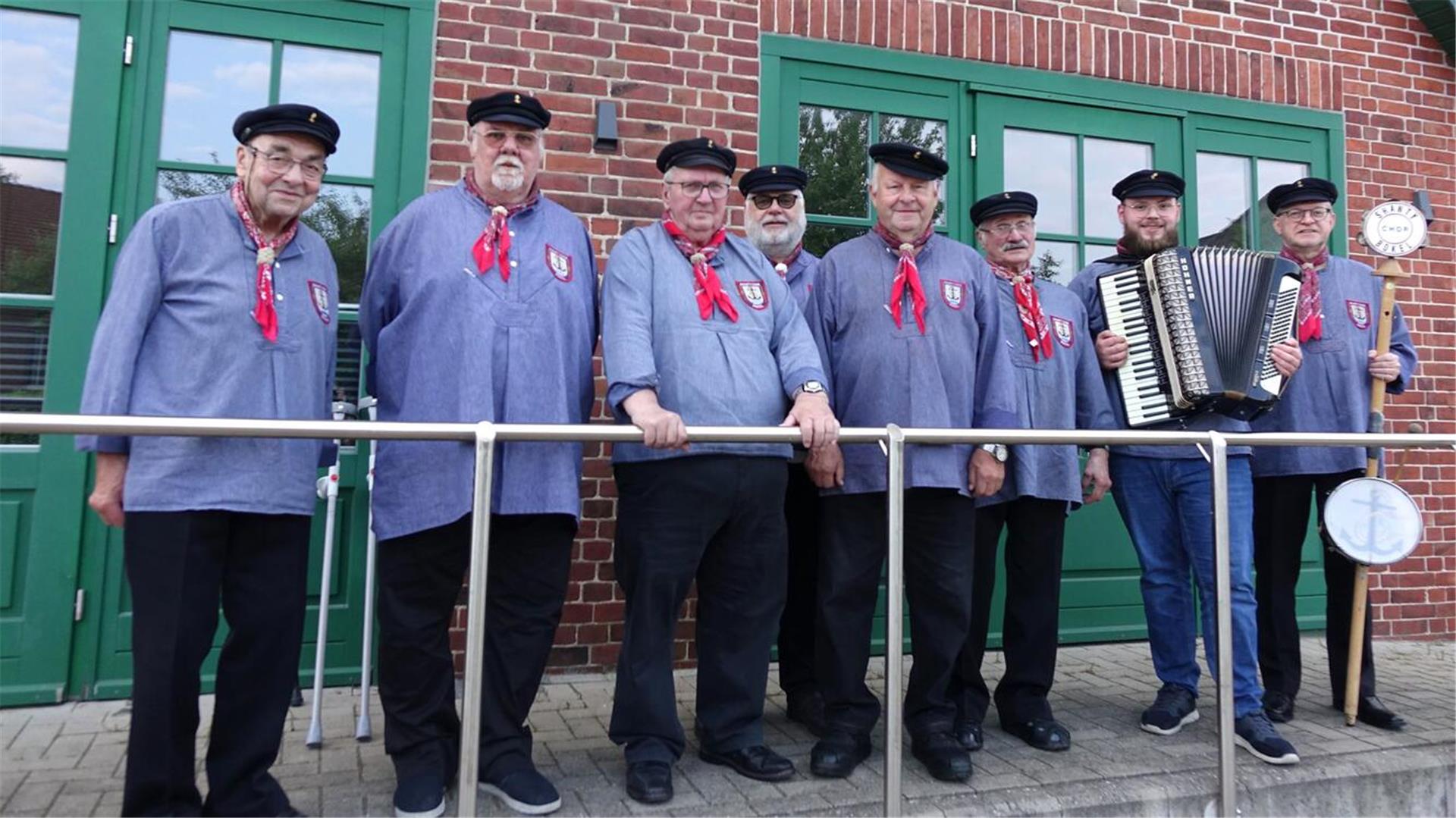 Das Foto zeigt acht Mitglieder eines Shanty-Chores in traditioneller Tracht. Der zweite Herr von rechts hält ein Akkordeon in den Händen.