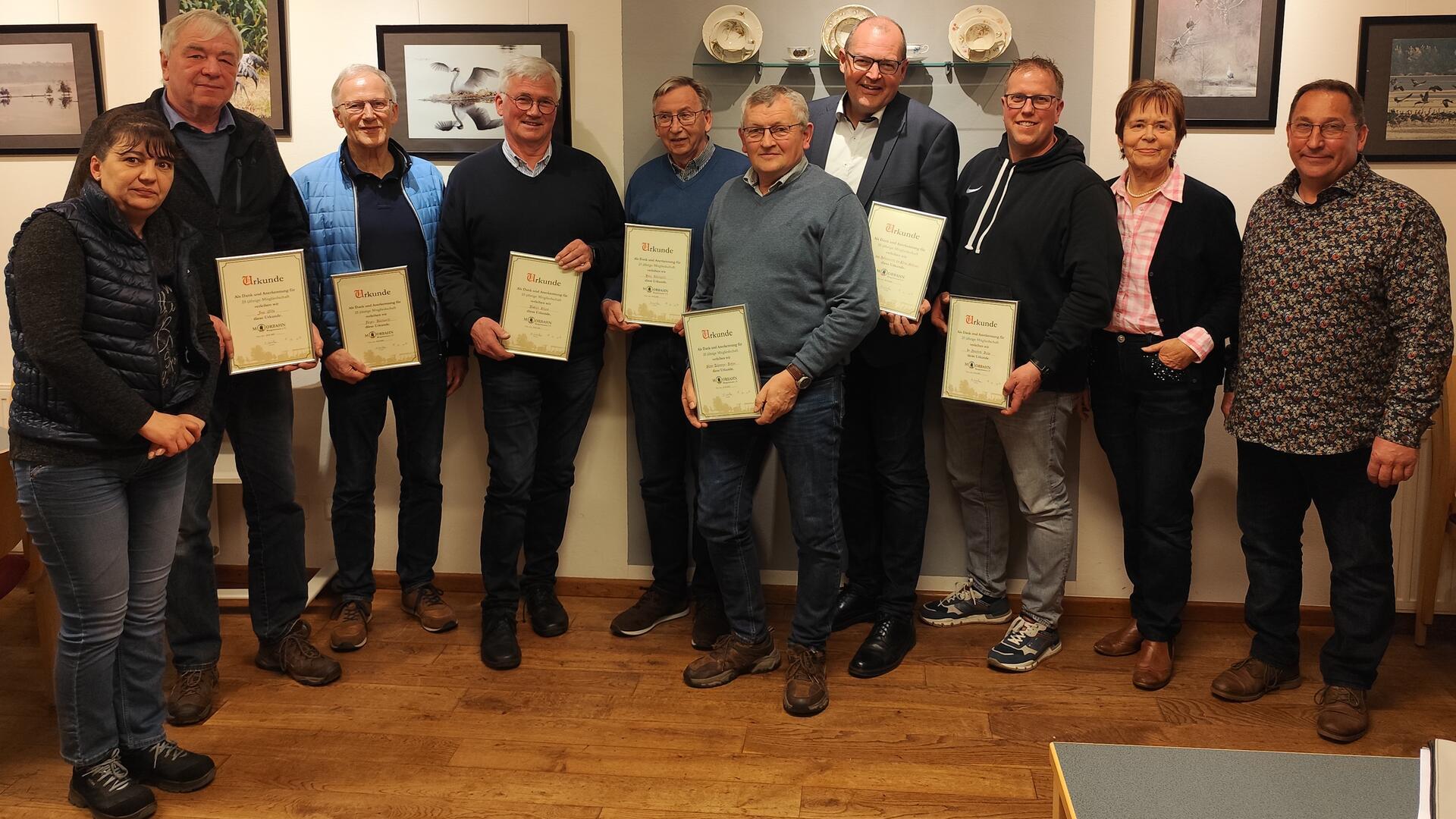 Männer und Fraauen mit Urkunden in der Hand stehen nebeneinander vor einer Wand.