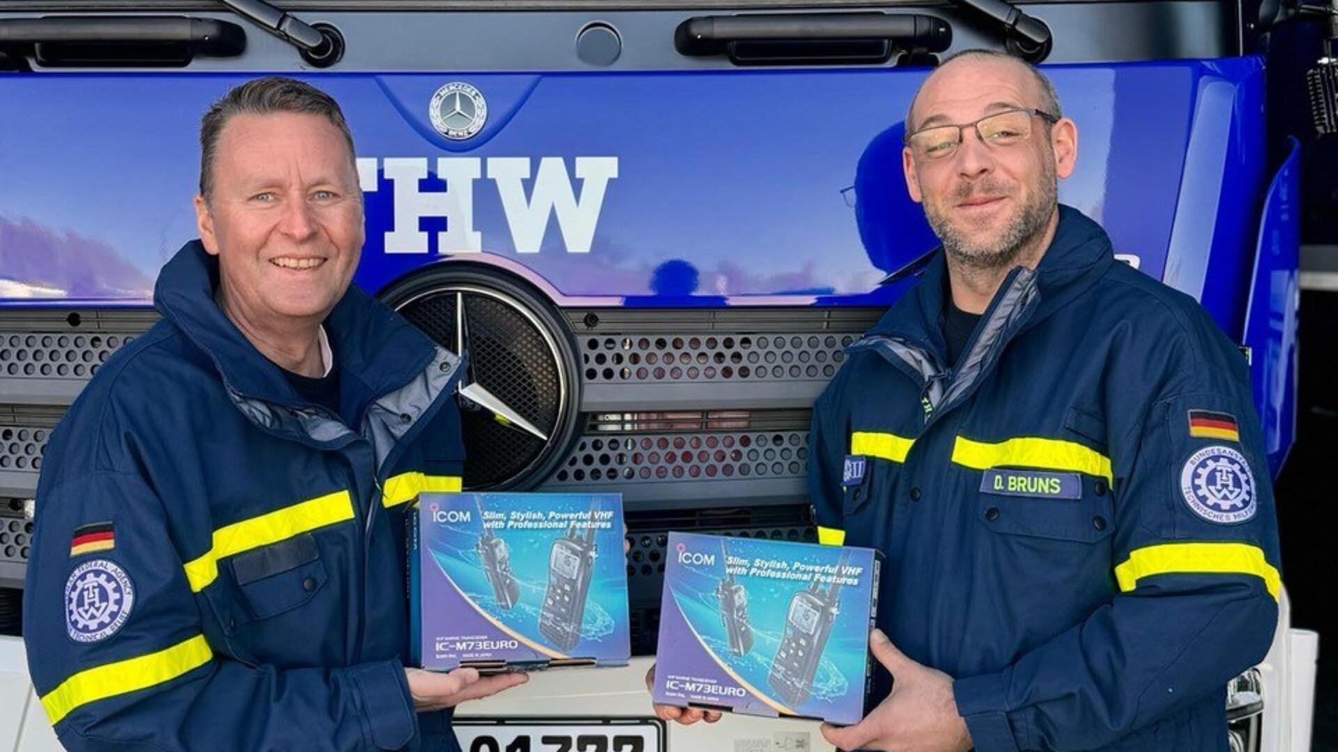 Zwei Männer stehen nebeneinander. In ihren Händen halten sie jeweils die Verpackung eines Seefunkgerätes.