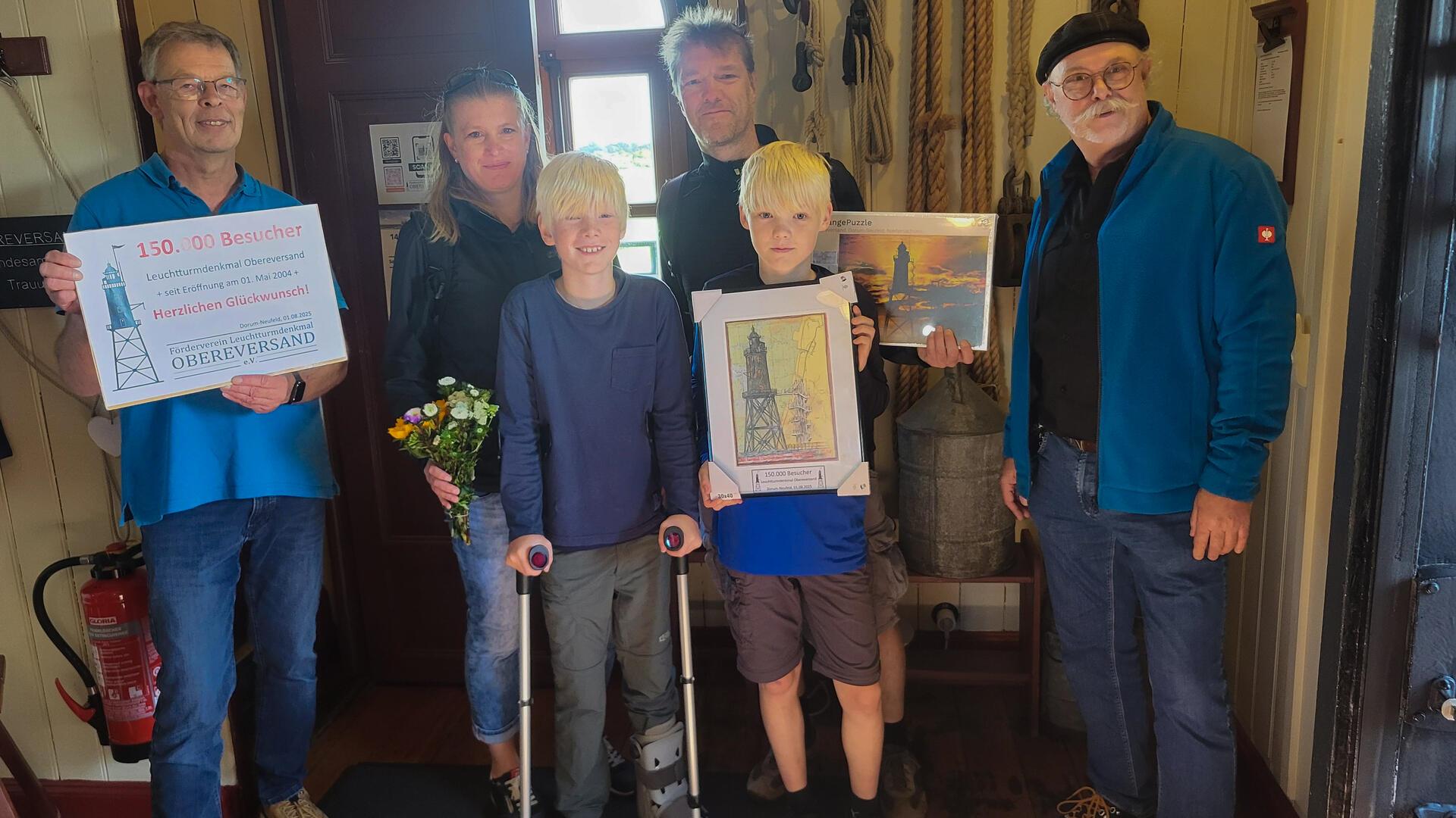 Kristian Pradel (links) und Gerit Moret (rechts) vom Förderverein Leuchtturmdenkmal Obereversand begrüßen Familie Becker aus bad Nenndorf als 150.000. Besucher des Turms.
