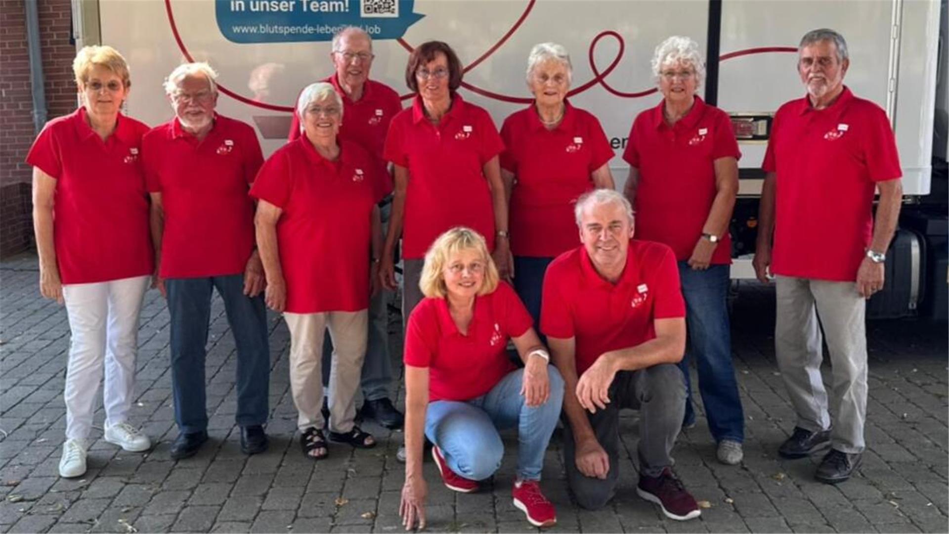 Gruppenfoto von zehn ehrenamtlichen Helferinnen und Helfern des DRK-Blutspendeteams Sievern in roten Poloshirts vor einem Blutspendewagen.