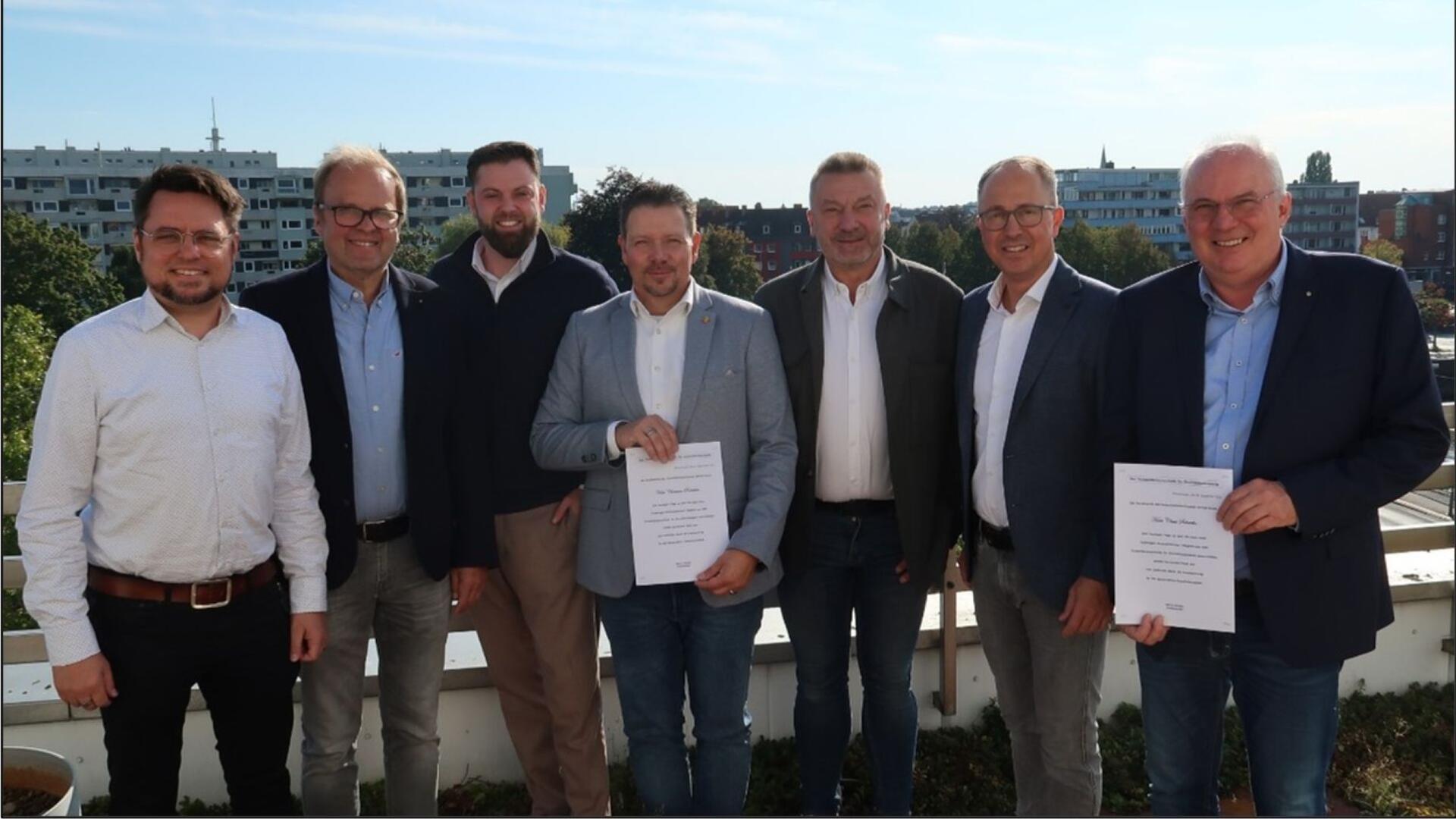 Gruppenbild mit sieben Männern. Zwei von ihnen halten eine Urkunde in den Händen.