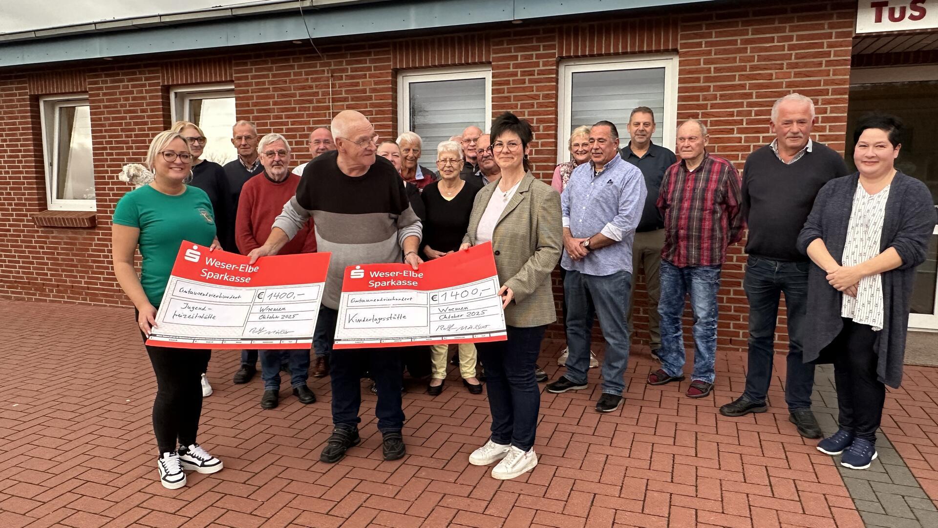Gruppenfoto von einer Spendenübergabe. Im Vordergrund halten drei Personen zwei symbolische Spendenschecks in die Höhe.