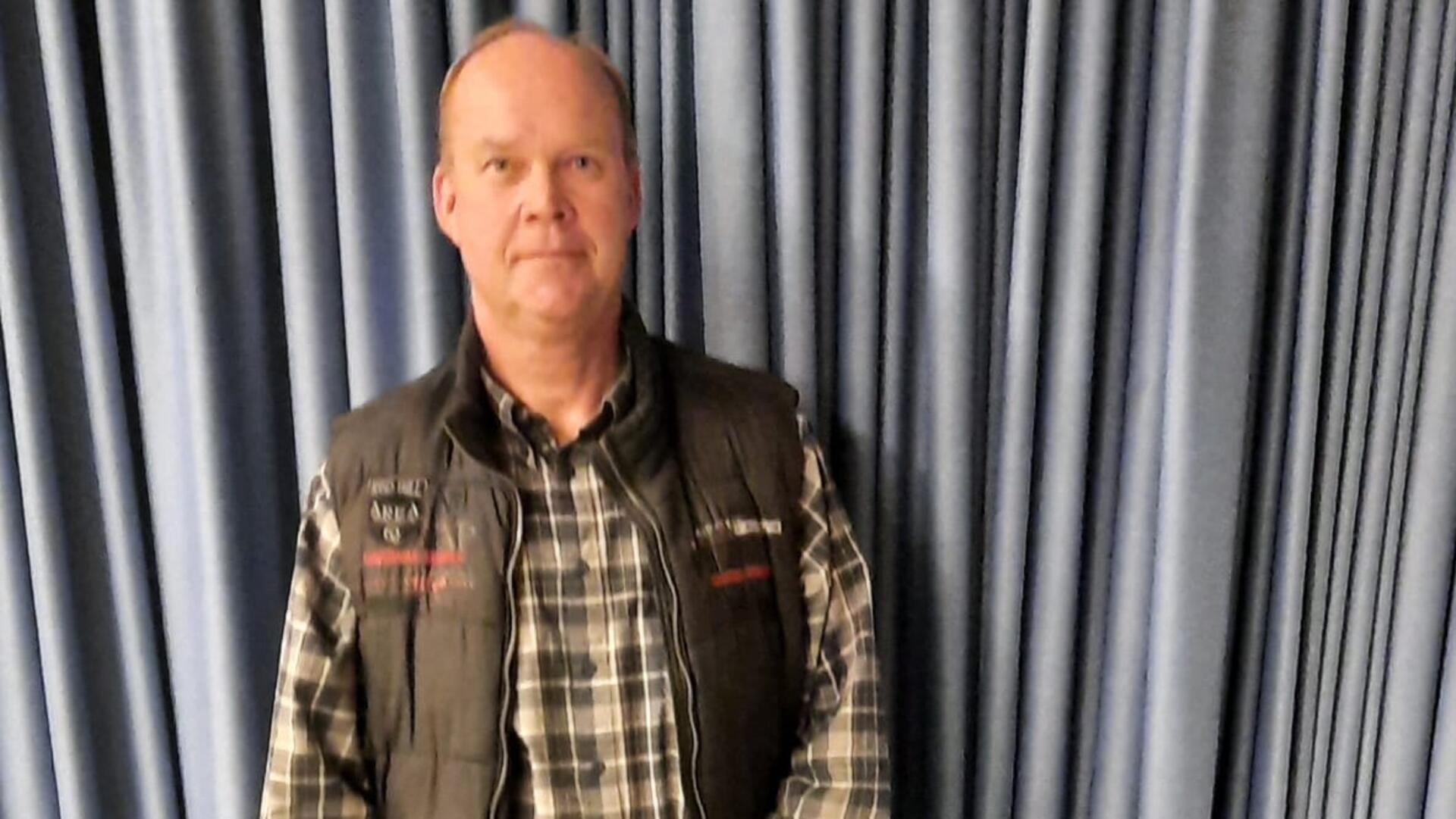 Ein Mann steht vor einem grauen Vorhang.