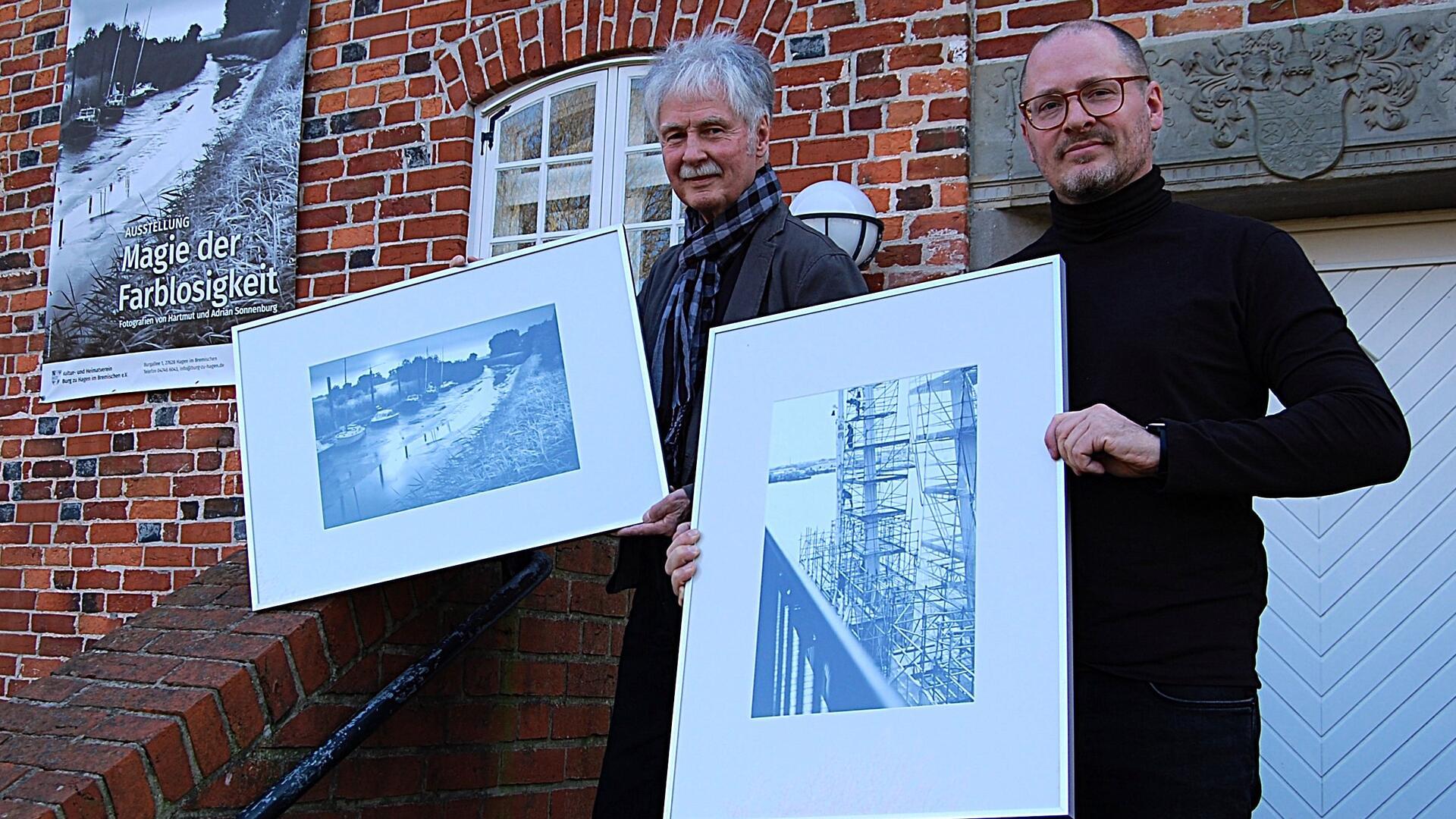 Zwei Männer zeigen jeweils ein großformatiges Foto.