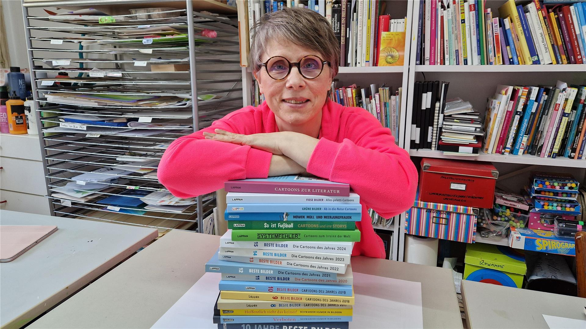 Eine Frau, auf einen Stapel Bücher gestützt, lächelt in die Kamera.