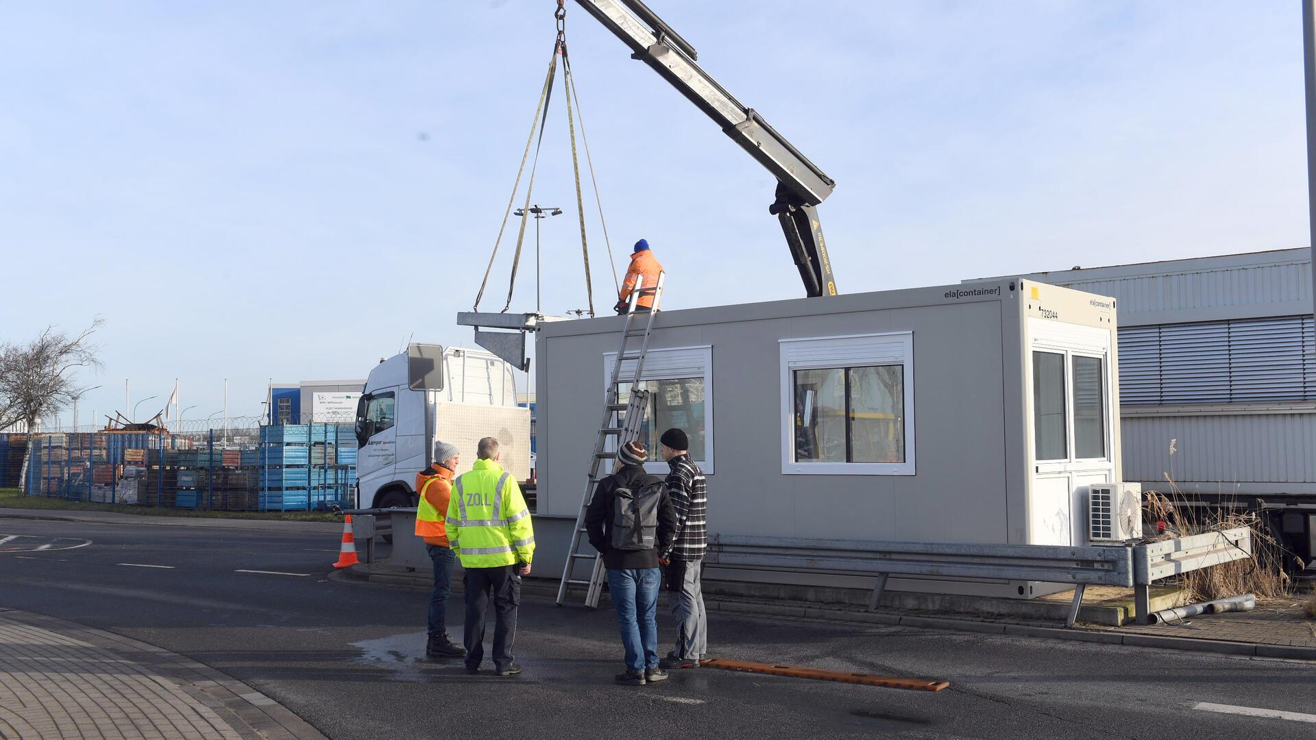 Männer stehen vor einem Baucontainer.