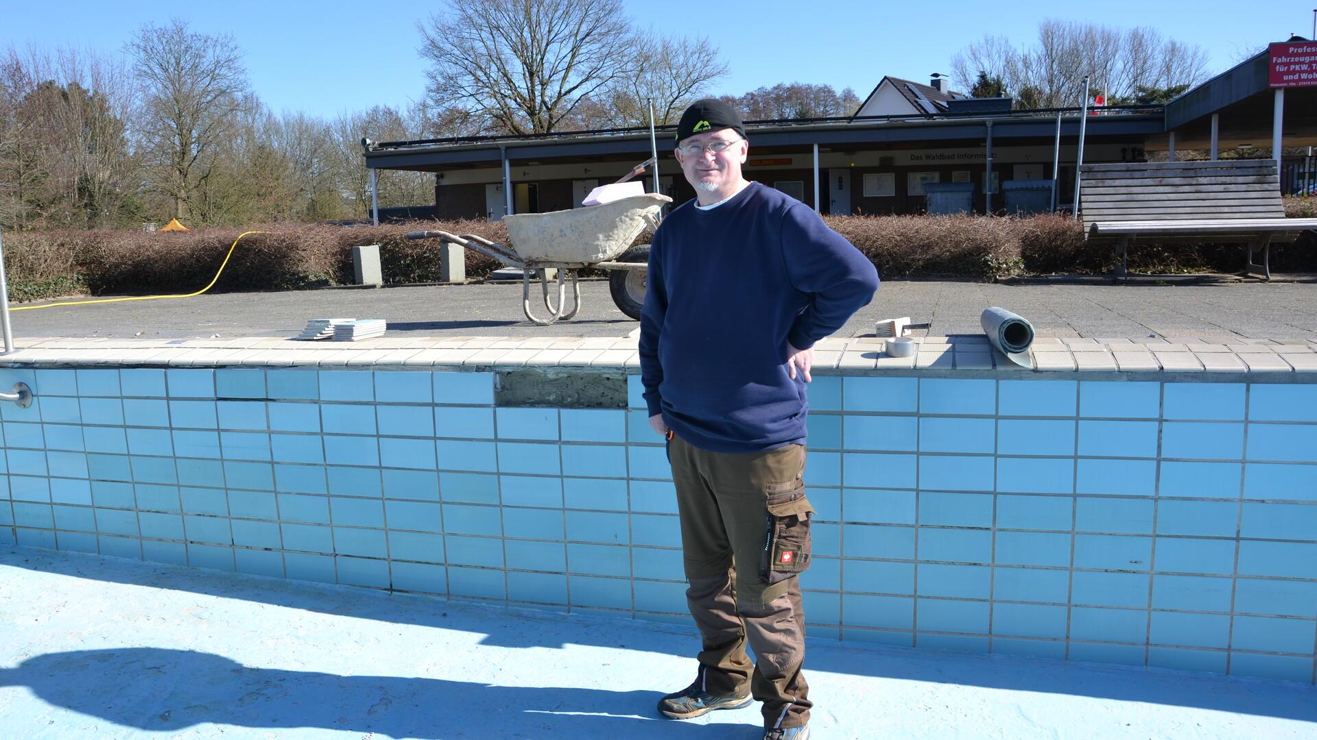 Ein Mann mit Sonnenmütze steht freundlich lächelnd in einem leeren Schwimmbecken neben einer Schadstelle.