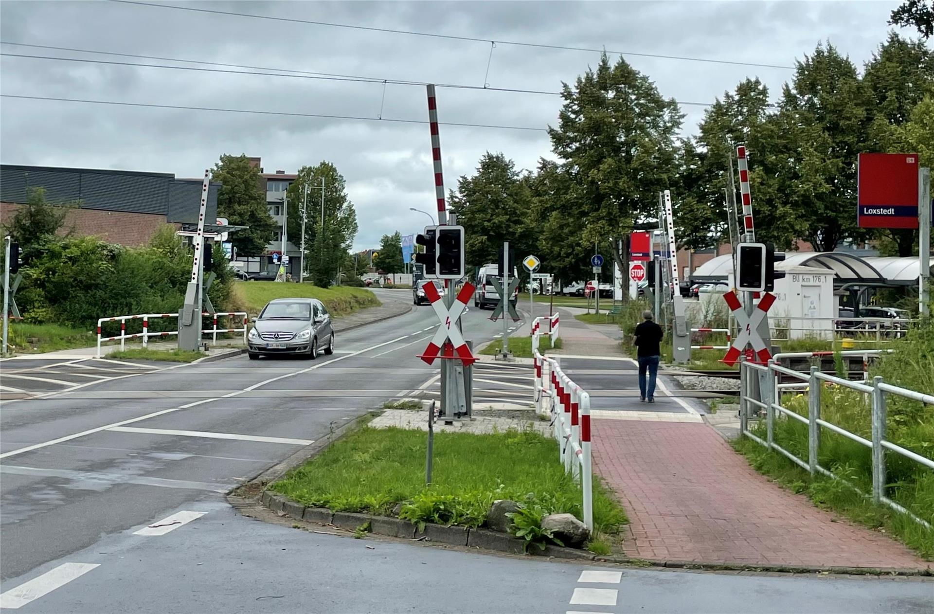 Ein Straße, auf der ein Auto fährt. Bahnschranken sind zu sehen, ebenso wie ein Fußgänger.