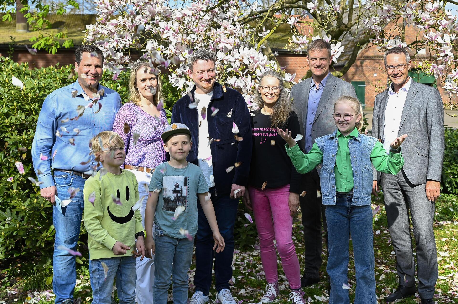 Gruppenfoto mit Erwachsenen und Kindern im Grünen. Blütenkonfetti für ein Vierteljahrhundert Opernkult (von links): Gastgeber Sönke und Sunhild Holsten, Adrian Rusnak (musikalischer Leiter), Moderatorin Martina von Ahsen, Carsten Hoops vom Niedersächsischen Landvolk und Stefan Hunsche vom Vorstand der Bremischen Volksbank Weser-Wümme freuen sich auf die nächste Auflage.