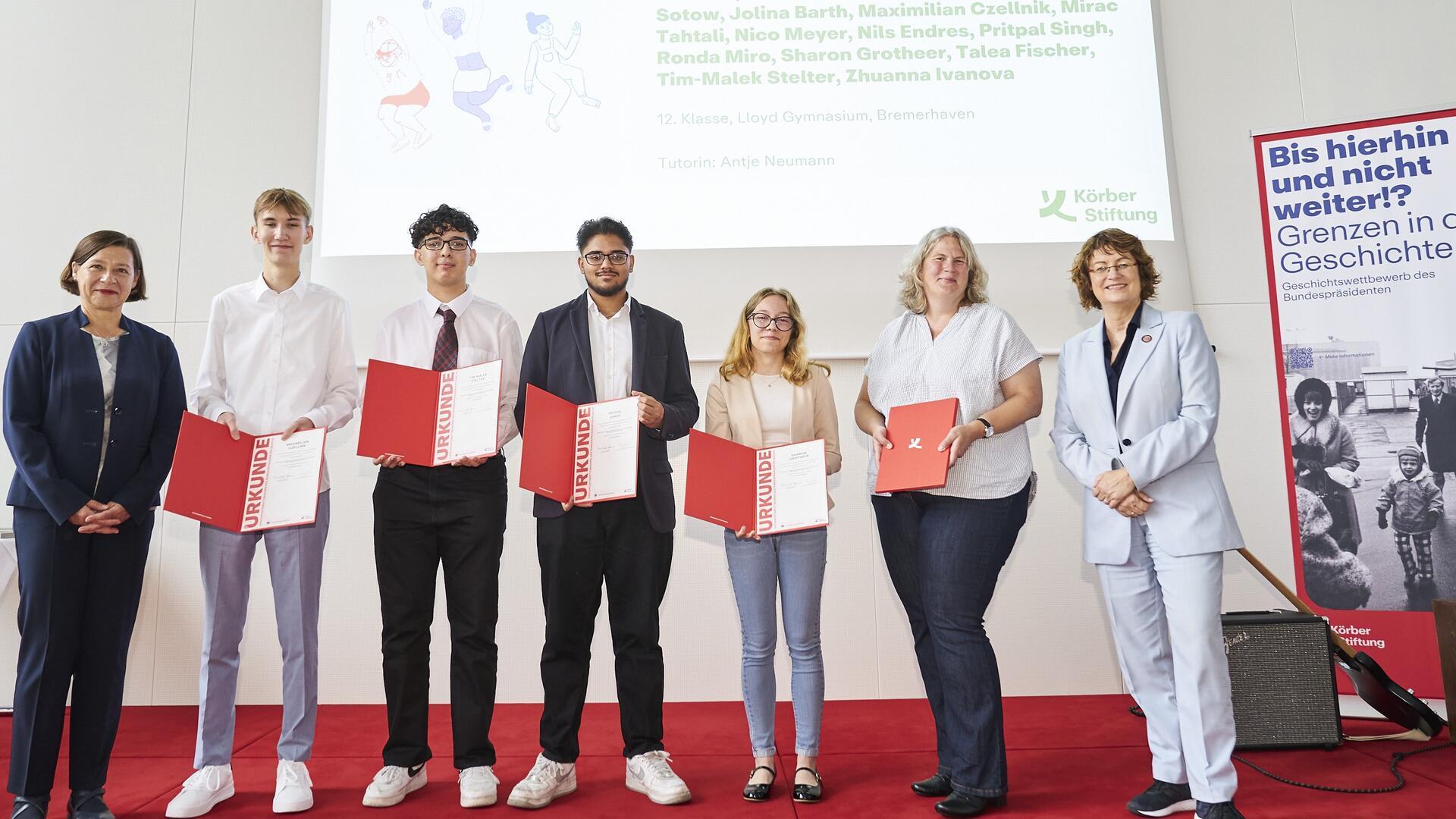 Mehrere Menschen stehen auf einer Bühne und halten Auszeichnungen in der Hand. 